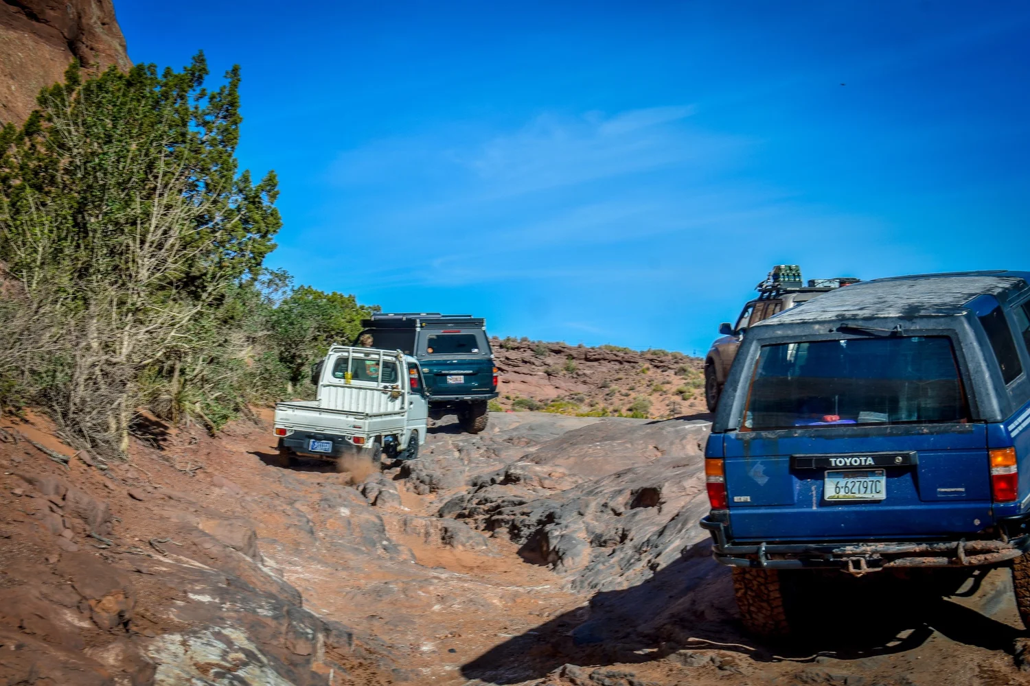 Blue second-generation Toyota 4Runner following a small white truck on a desert trail at Cruise Moab