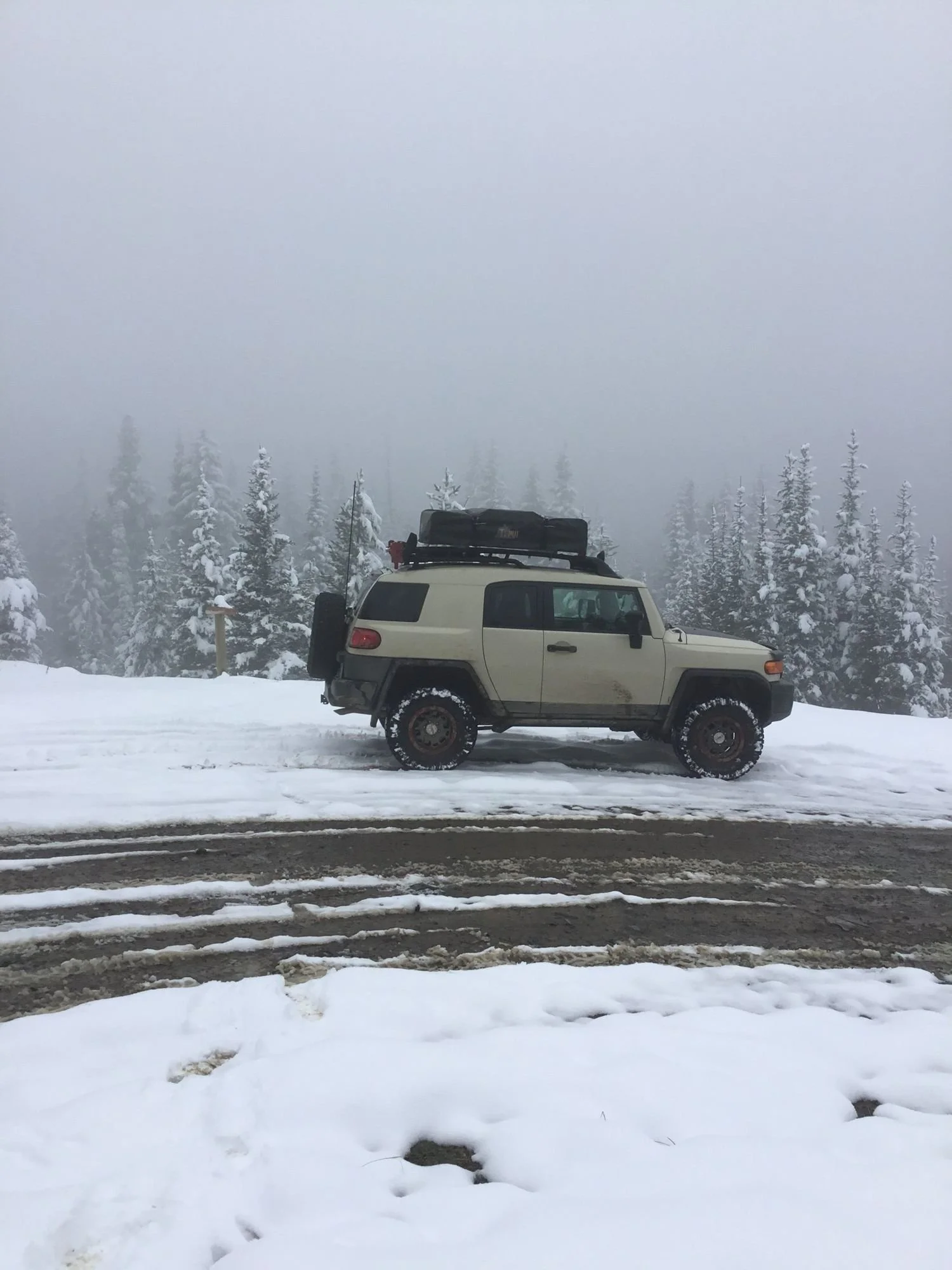 Tan FJ Cruiser parked on a snowy hilltop in fog on Little Bear Road in the Gallatin Range near Bozeman, Montana