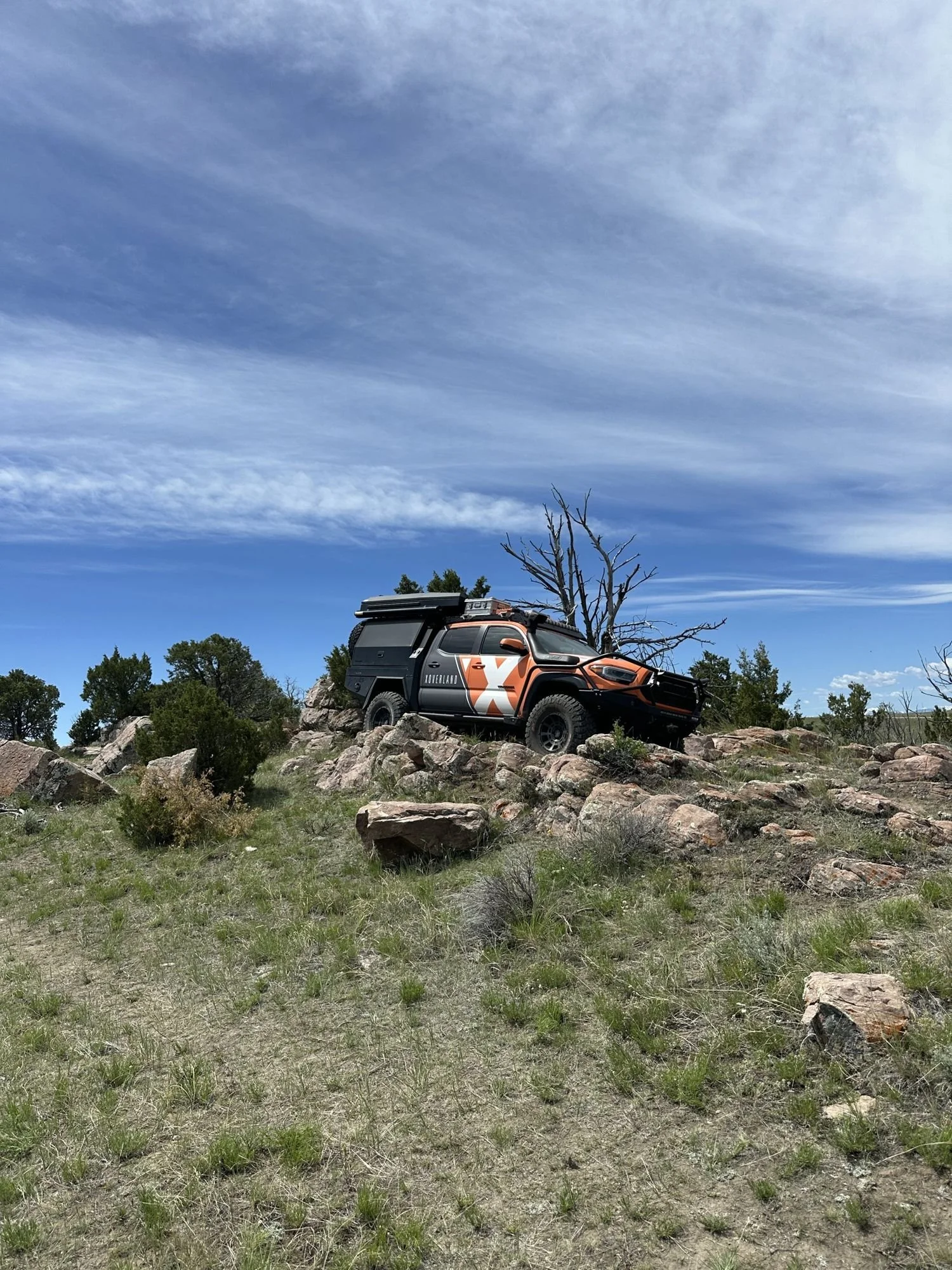 Tacoma with a camper and orange X wrap parked among rocks at XOverland Ranch near Bozeman, Montana