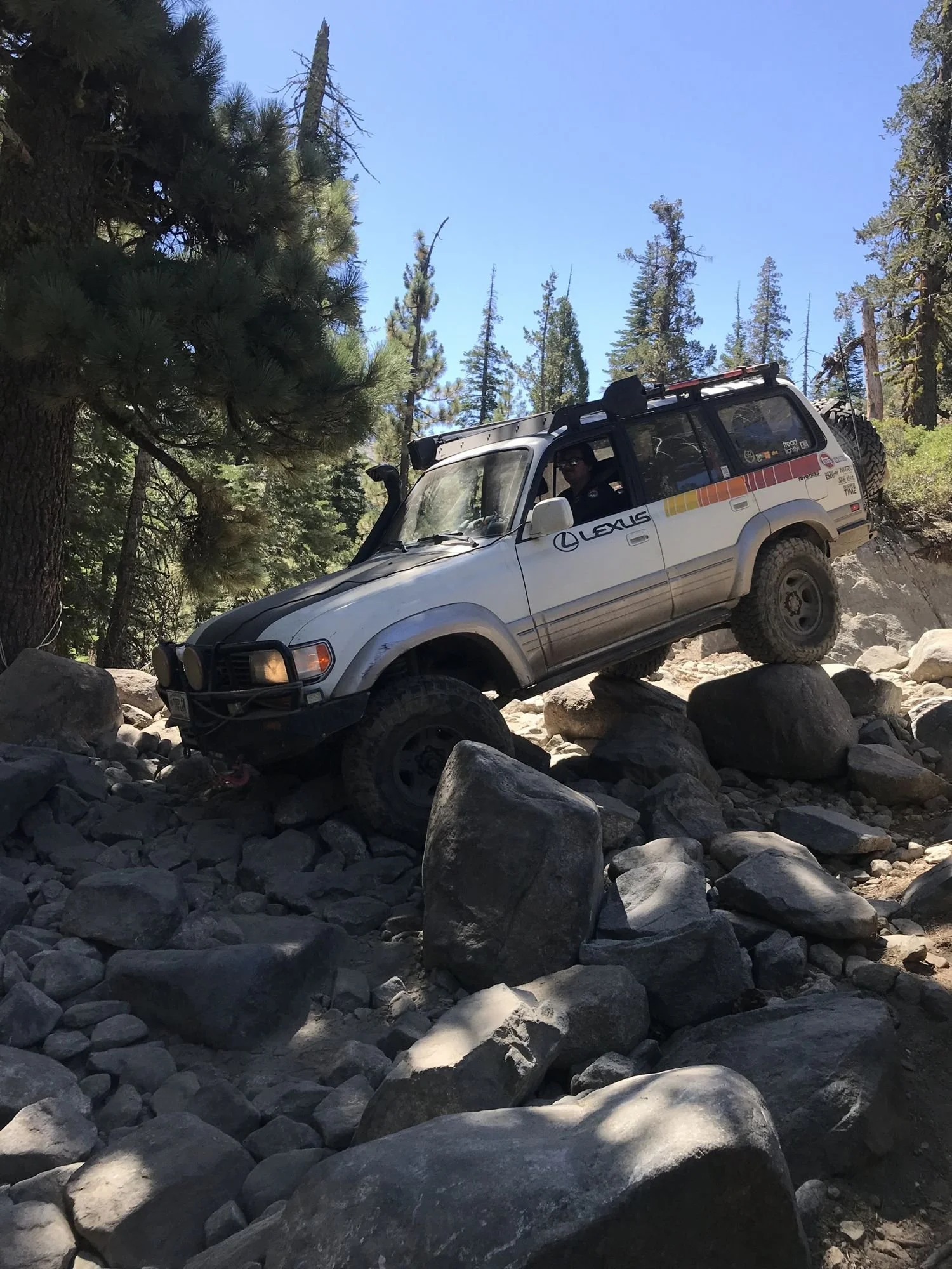 Silver Lexus LX450 with retro stripes crawling over large granite boulders in the pines on the Rubicon Trail in California during Rubithon 2022