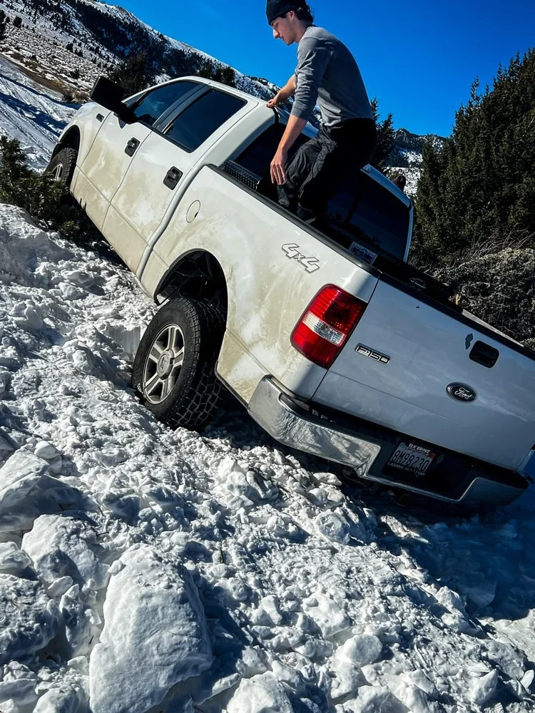 A white Ford F-150 slid sideways into a snow-filled ditch while a man stands in the bed