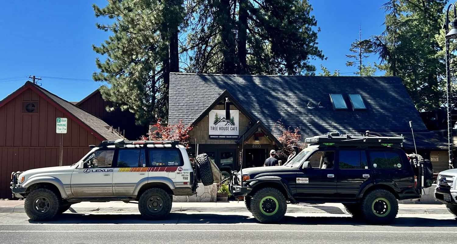 Striped Lexus LX450 and a black Land Cruiser with green wheels parked outside a wooden cafe in the pines after the Rubicon Trail