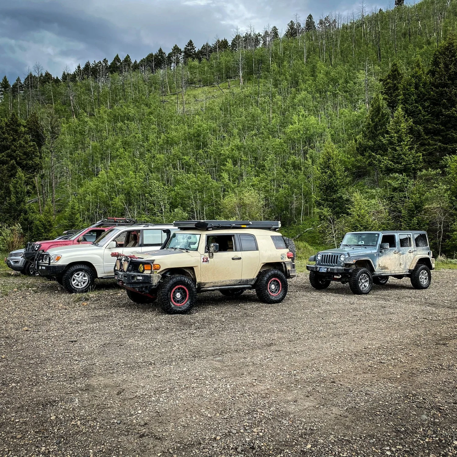Tan FJ Cruiser, white Land Cruiser, Jeep Wrangler and a red SUV lined up on a gravel pullout in the Elkhorn Mountains near Boulder, Montana