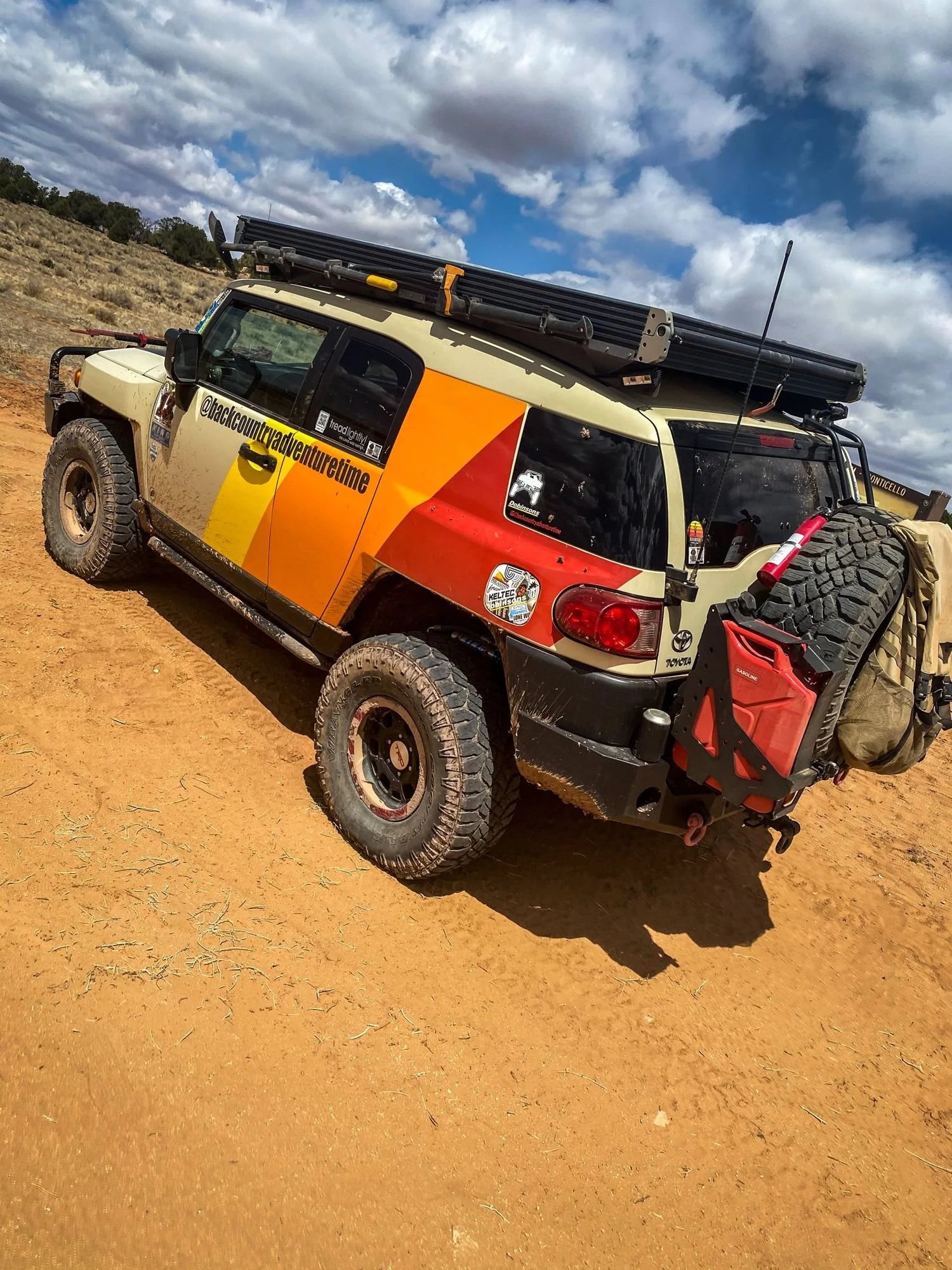 Tan Toyota FJ Cruiser with orange and red retro stripes on red sand under a cloudy sky on a spring road trip through Utah