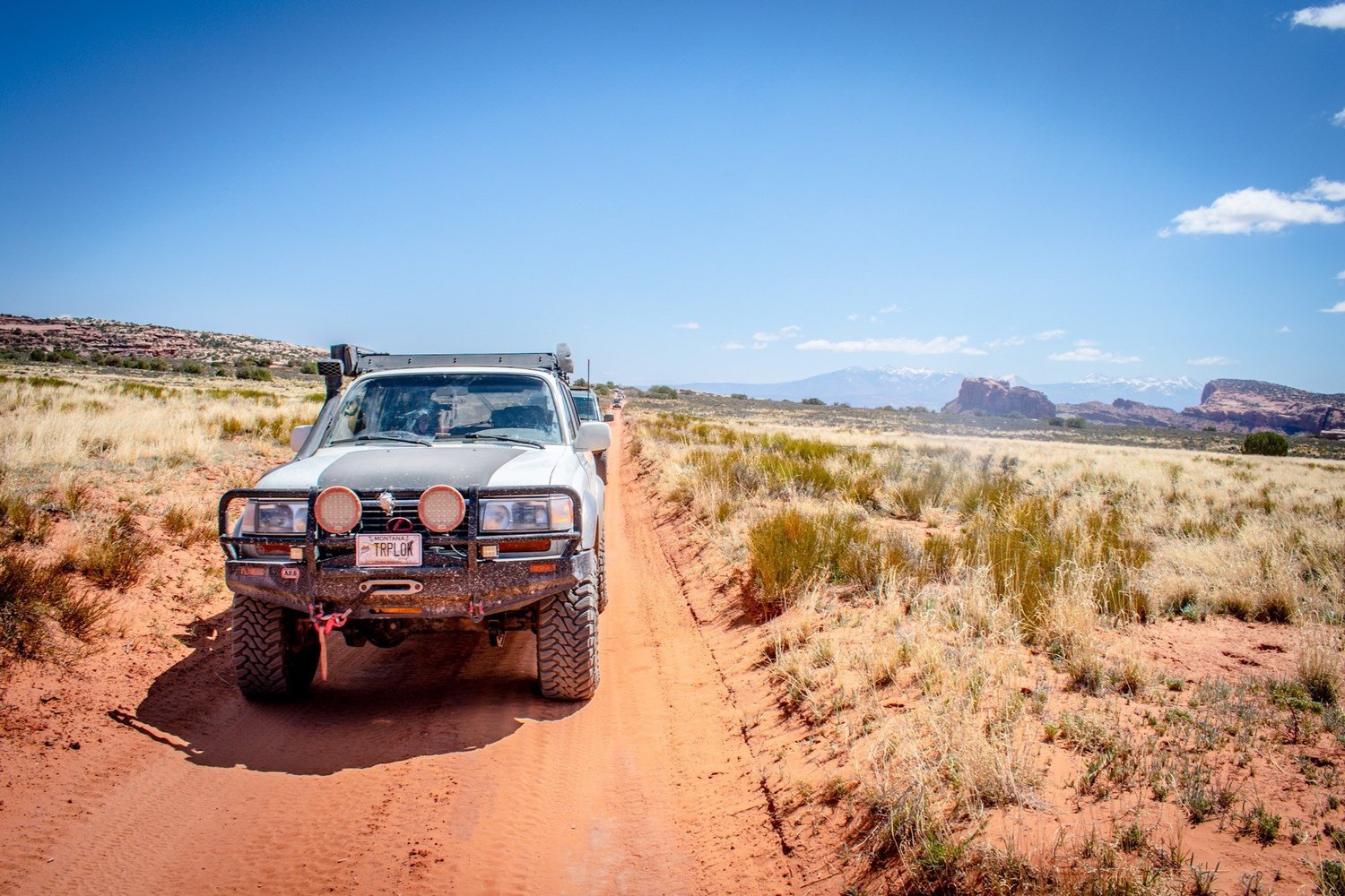 Silver Lexus LX450 TRPLOK with a dark hood, ARB bumper, round lights and a snorkel on a red dirt road on the Seven Mile Rim trail near Moab, Utah