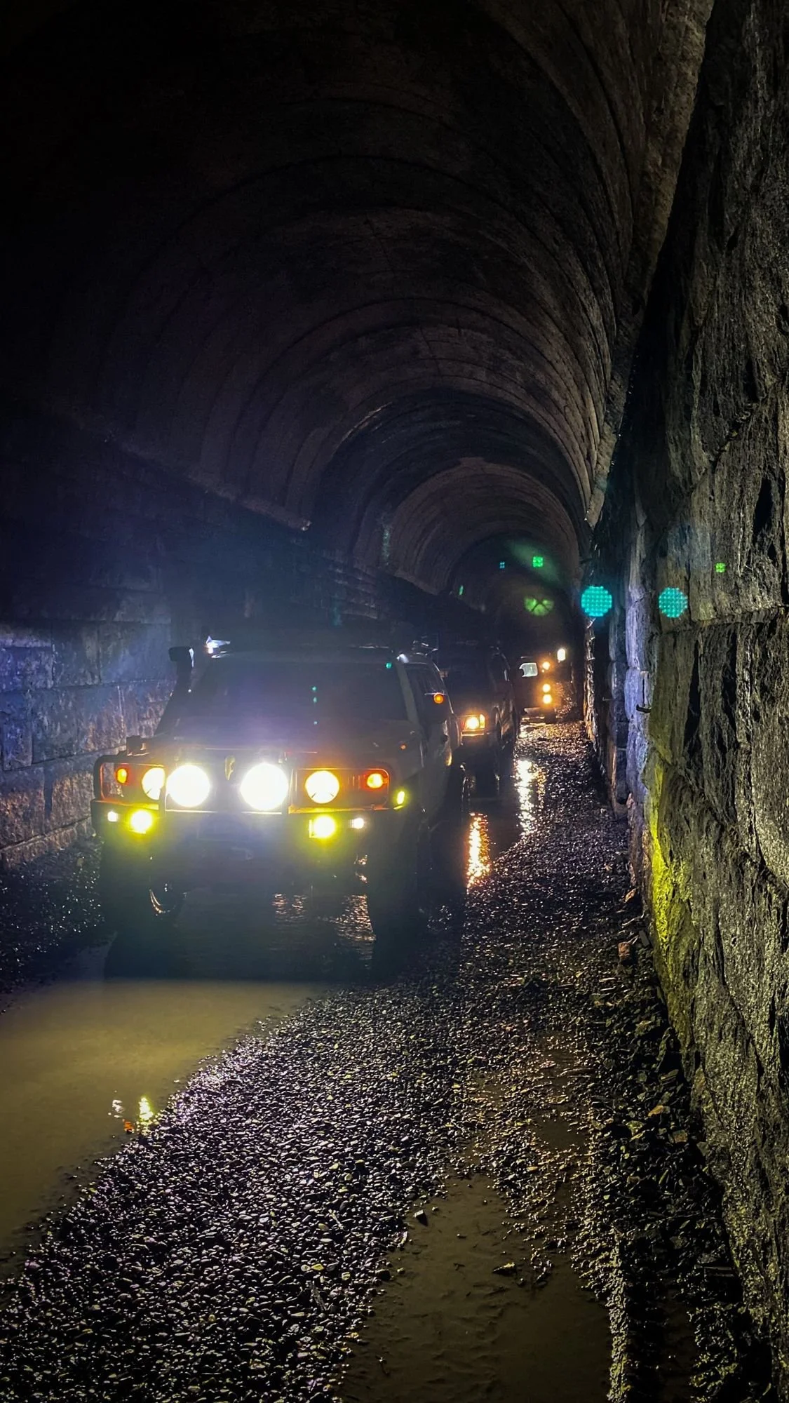 Off-road truck with yellow and white lights glowing inside the dark stone-lined Wickes railroad tunnel at the Wickes railroad tunnel near Jefferson City, Montana