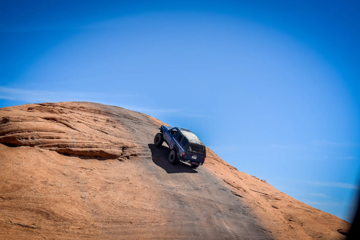 Toyota 4Runner climbing a slickrock face under a blue sky at Cruise Moab