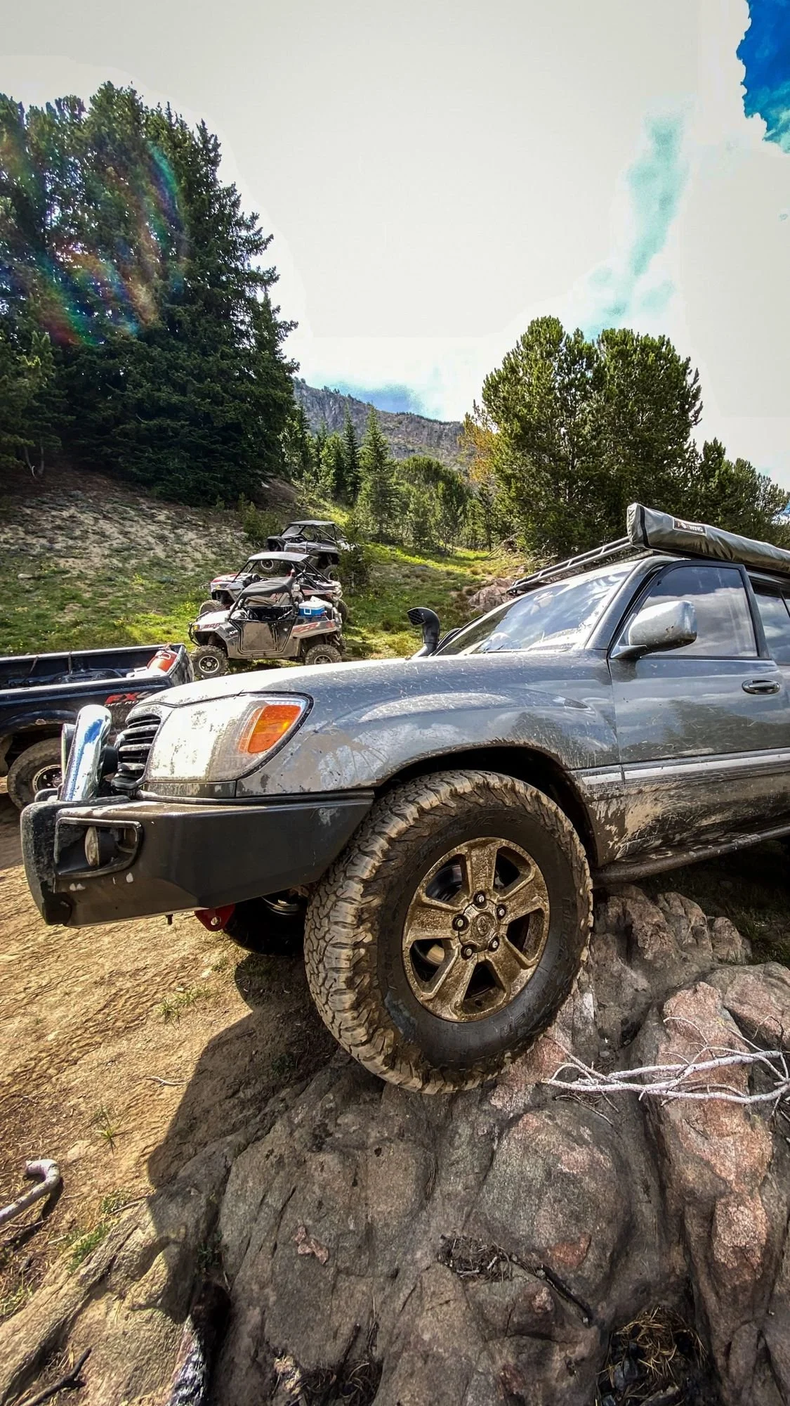 Gray Toyota Land Cruiser with its front tire perched on a large rock on the Independence road above the Boulder River, Montana