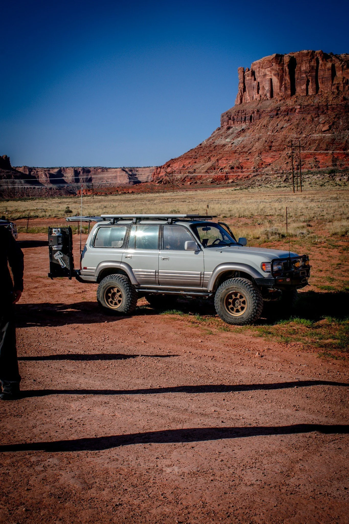 Champagne Land Cruiser 80 Series wagon with a swing-out carrier below a butte in early light on the Seven Mile Rim trail near Moab, Utah