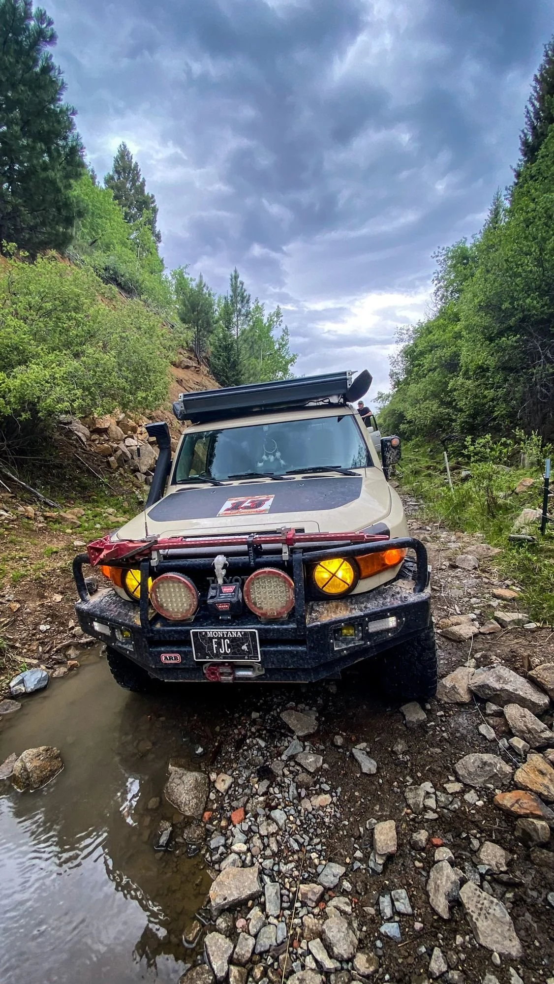 Tan Toyota FJ Cruiser with amber lights and a steel bumper parked in puddles on the rocky Wickes tunnel approach at the Wickes railroad tunnel near Jefferson City, Montana