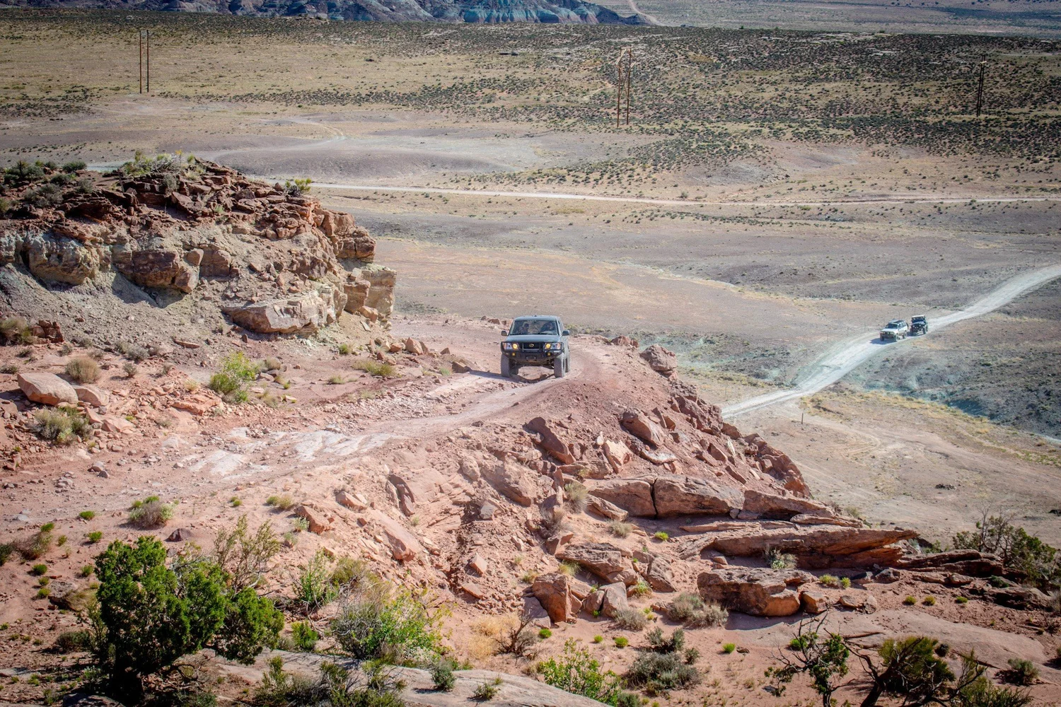 High view of a truck on a descent and another on a dusty two-track below on the Seven Mile Rim trail near Moab, Utah