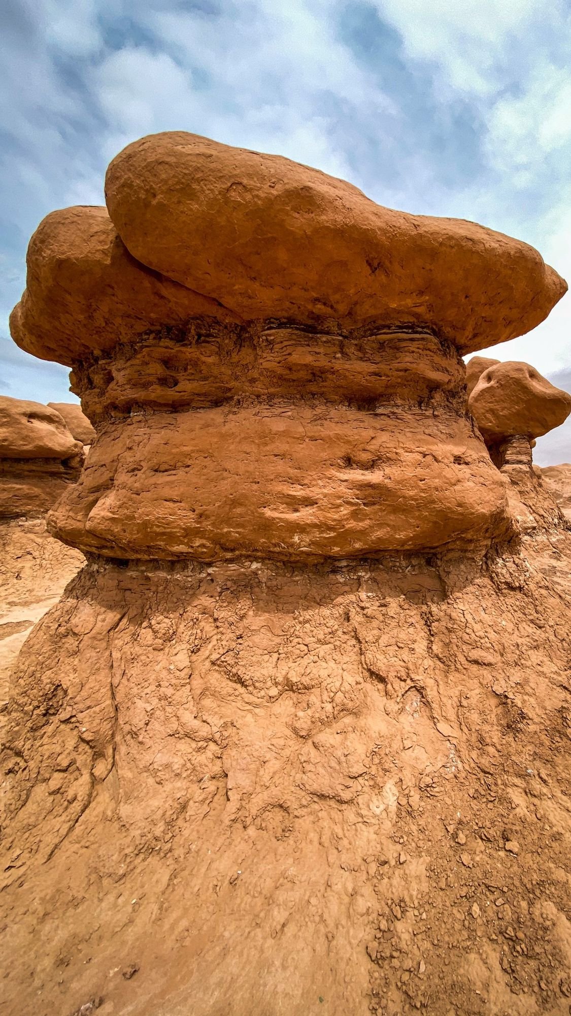 Mushroom-shaped red sandstone hoodoo with a wide cap under a cloudy sky in Goblin Valley State Park, Utah