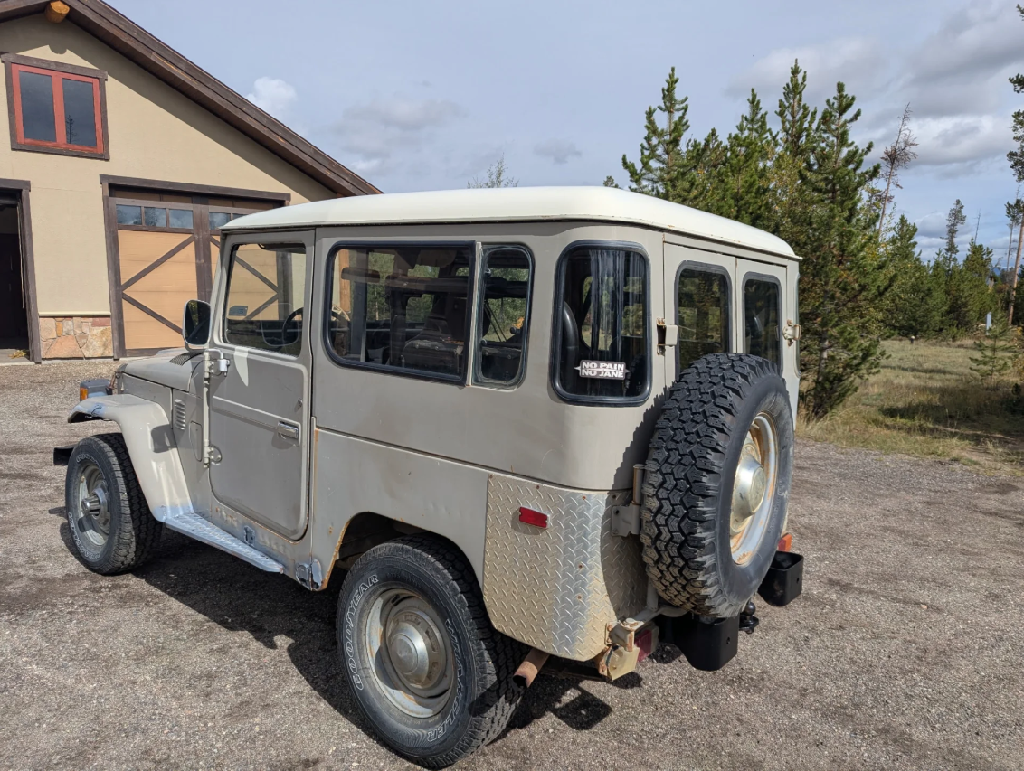Rear three-quarter view of the beige 1977 Toyota FJ40 with barn doors and spare tire