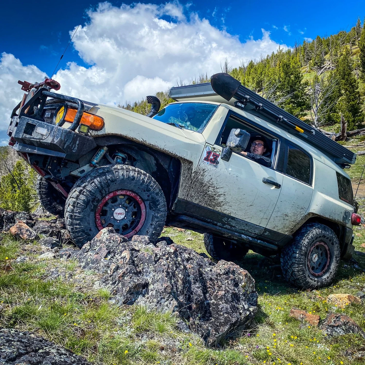 Tan Toyota FJ Cruiser climbing nose-up onto a rock outcrop under a blue sky in the Elkhorn Mountains near Boulder, Montana