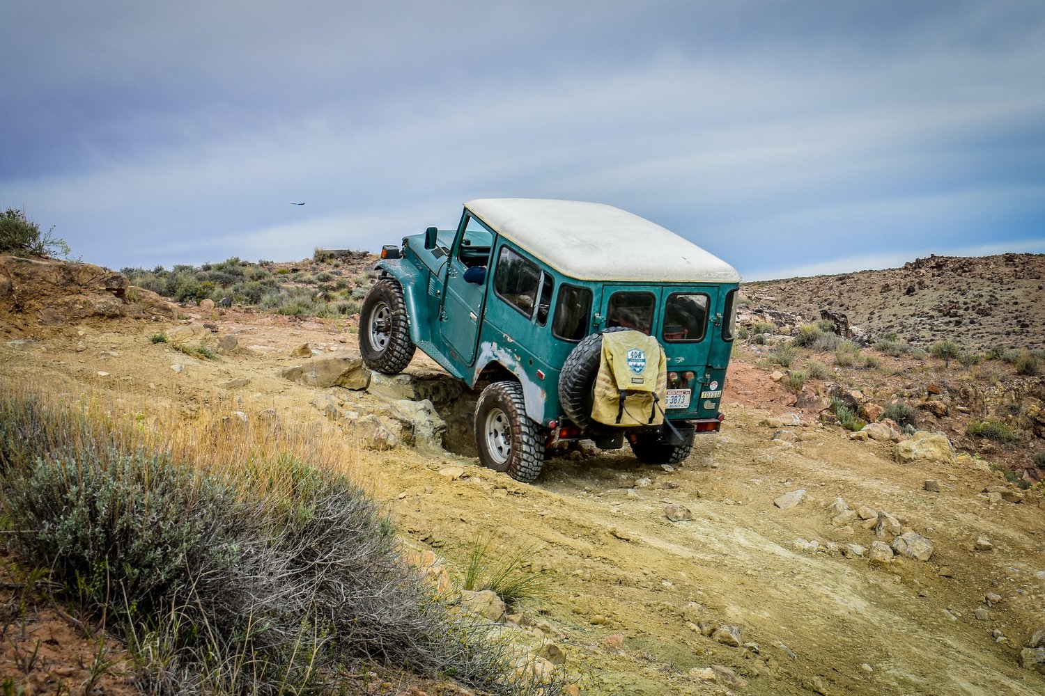 Teal Toyota FJ40 Land Cruiser with a white top crossing slickrock on the 3D Trail at Cruise Moab