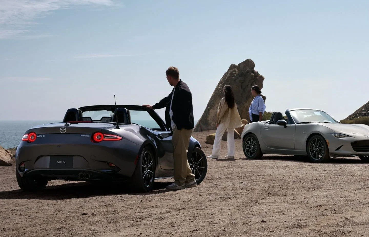 Two 2026 Mazda MX-5 Miata roadsters with their tops down on a coastal overlook