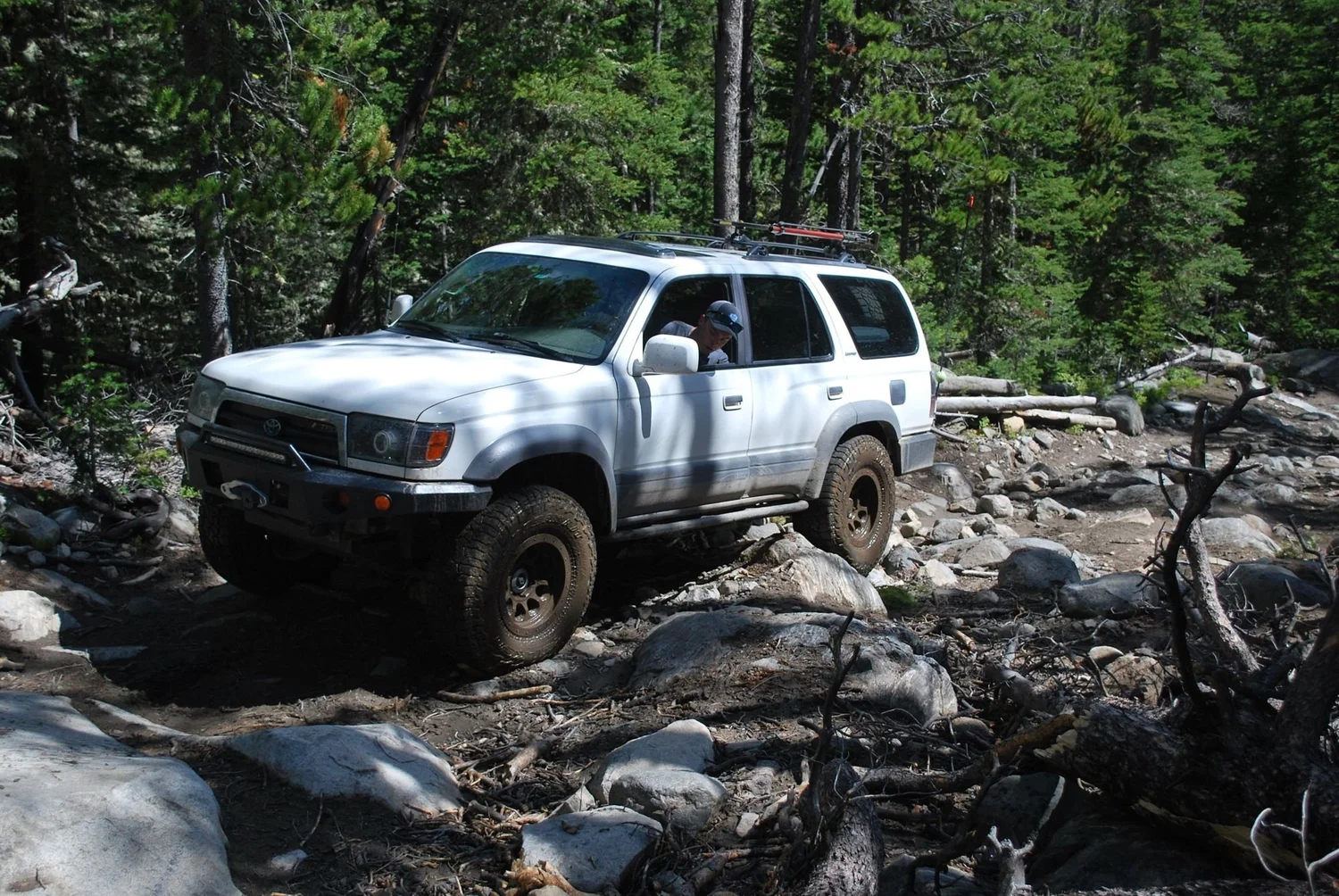 White 4Runner side-on in a boulder field in the trees on the North Meadow Creek Twin Lakes trail in the Tobacco Root Mountains, Montana