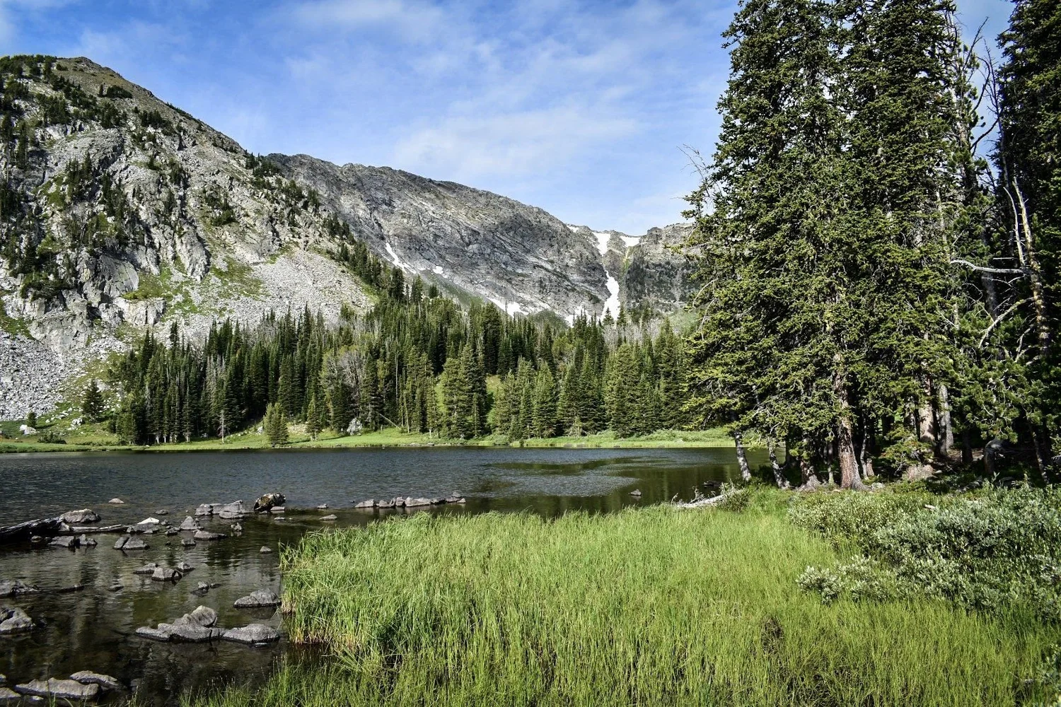 High lake below a rocky cirque with snow patches and pines on the North Meadow Creek trail to McKelvey Lake in the Tobacco Root Mountains, Montana