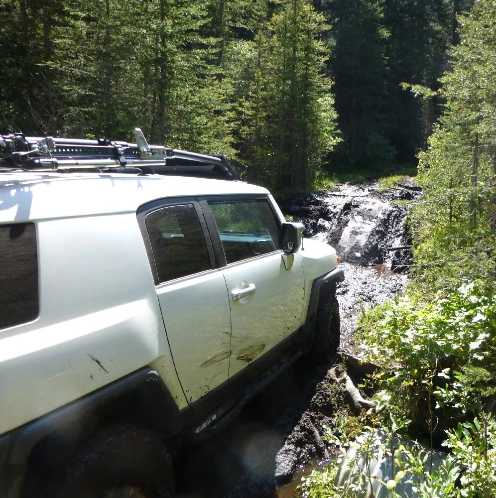 Silver FJ Cruiser alongside a small cascading creek in the trees