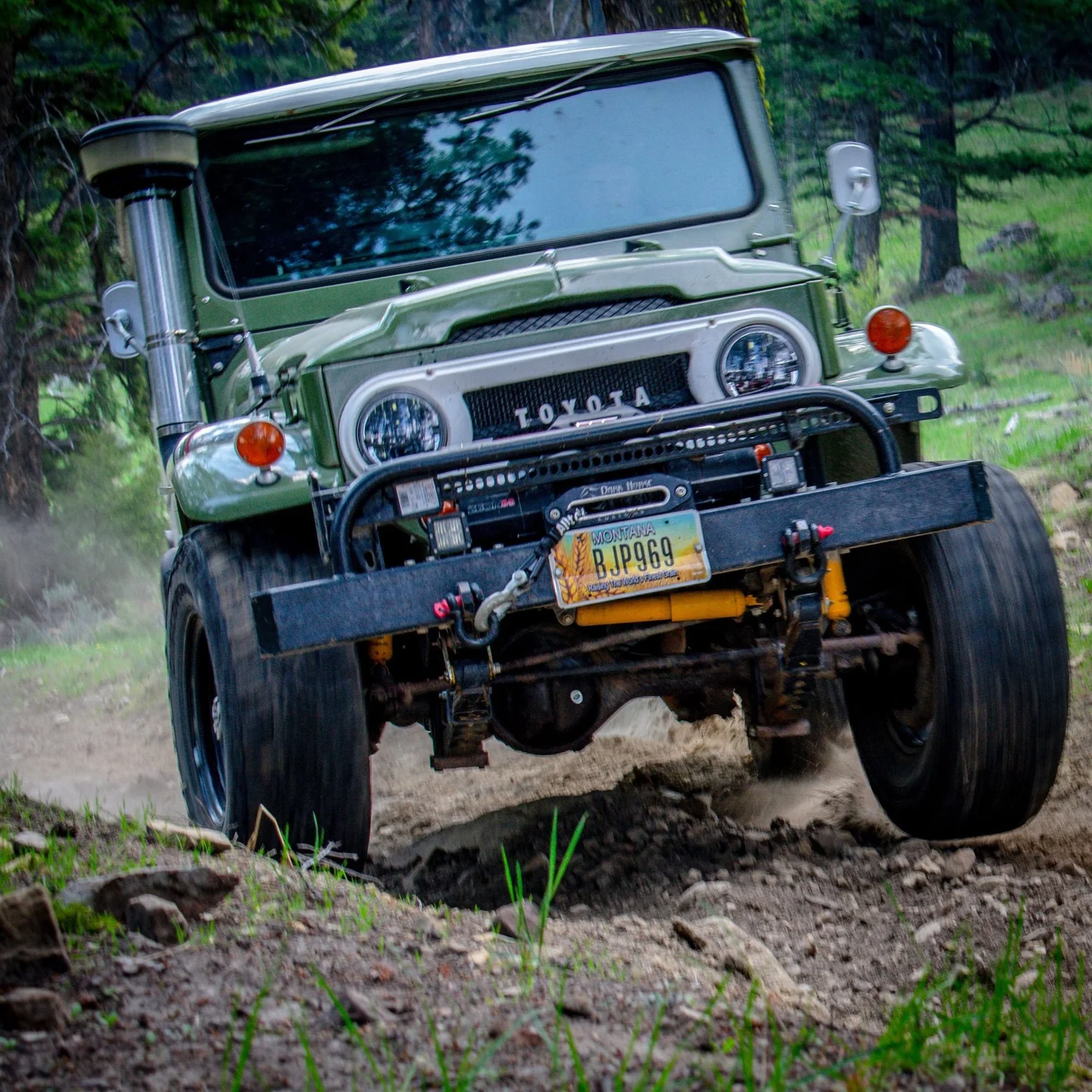 Green Toyota FJ40 Land Cruiser with a snorkel and winch, front tire lifting on a rocky trail on the Ringing Rocks trail near Pipestone, Montana