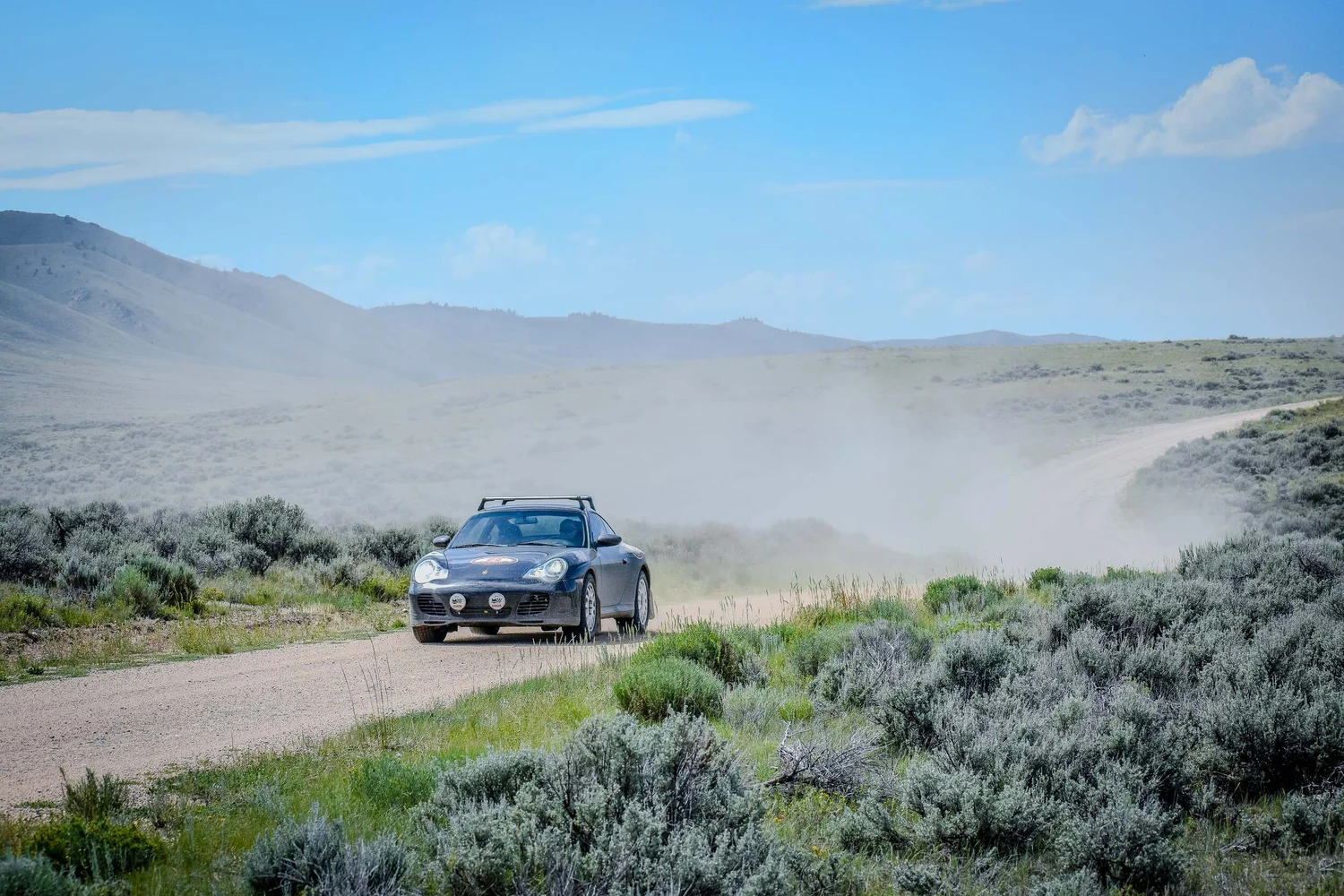 Blue wagon charging through a cloud of dust on a Montana backroad