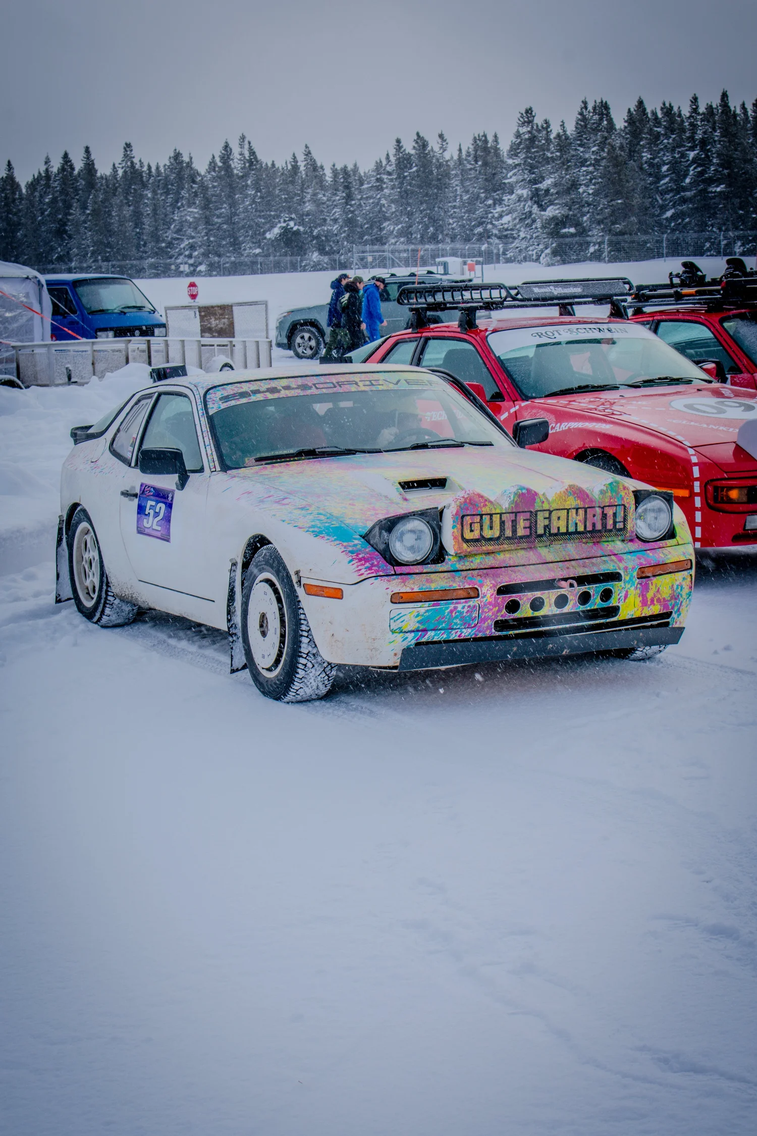 Porsche 944 with paint-splatter livery and Gute Fahrt banner at the Frost and Furious ice races in West Yellowstone