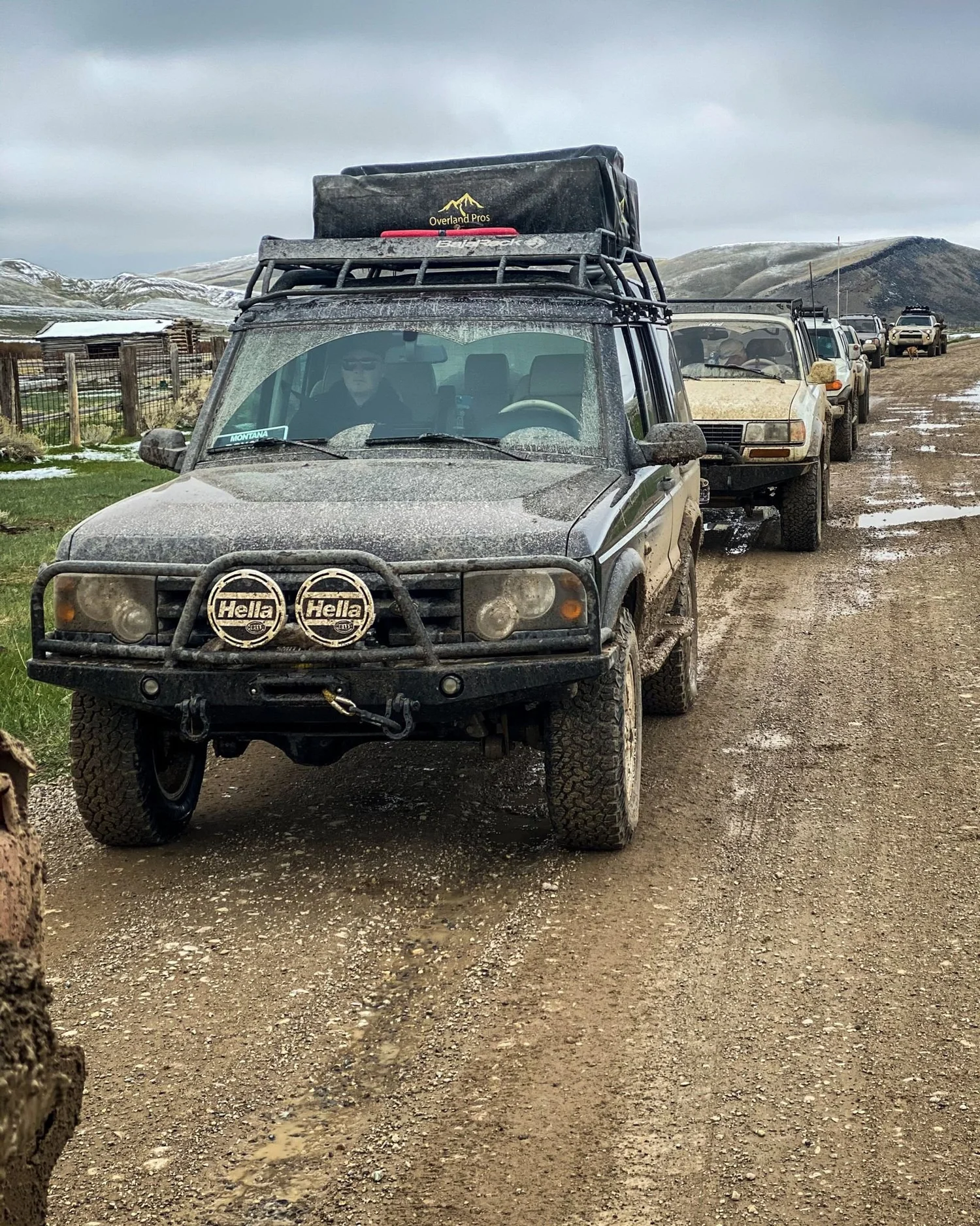 Dark green Land Rover Discovery leading a line of trucks on a muddy dirt road on a 406 Cruisers run in the upper Ruby River country, Montana
