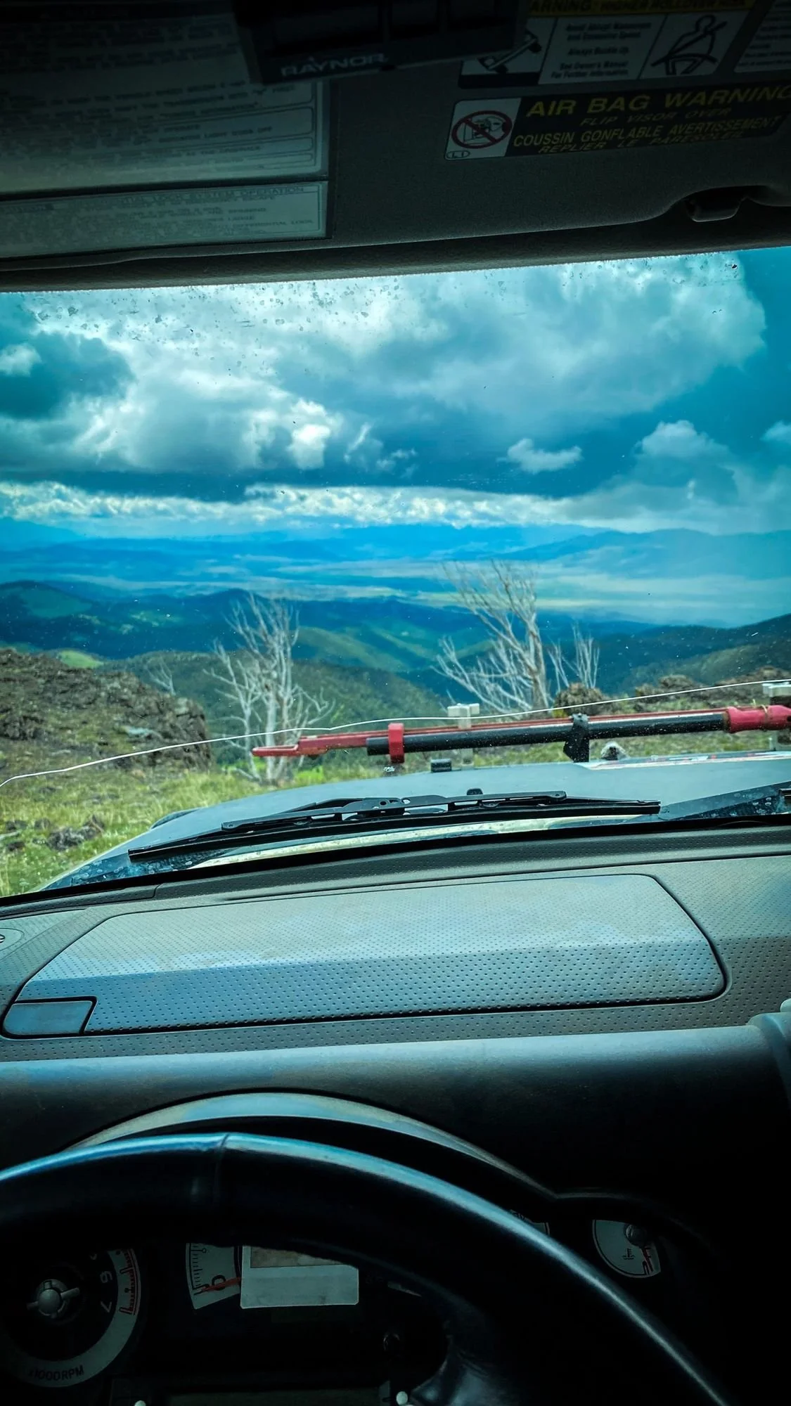 View through a truck windshield over a wide valley and distant mountains under big clouds in the Elkhorn Mountains near Boulder, Montana