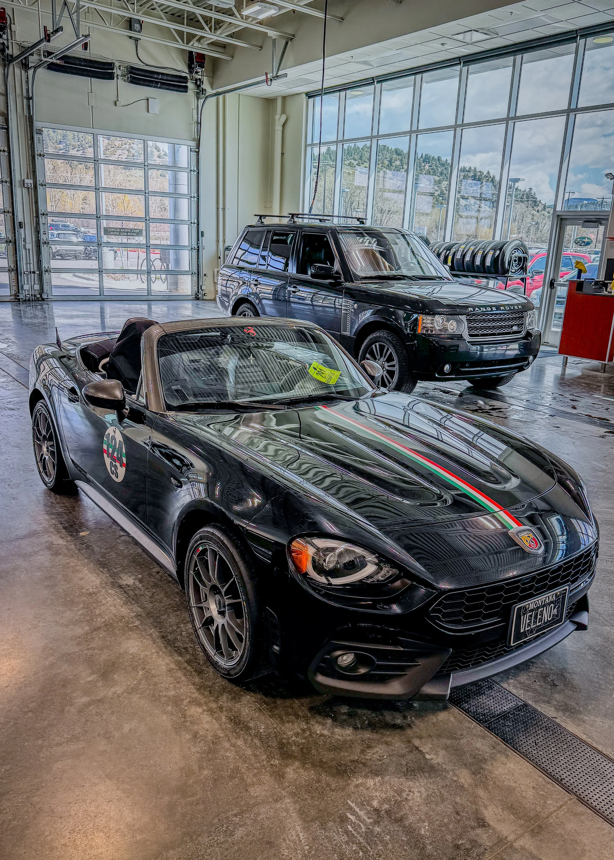 Front three-quarter view of the black Abarth 124 Spider showing the Italian tricolor hood stripe and VELENO plate