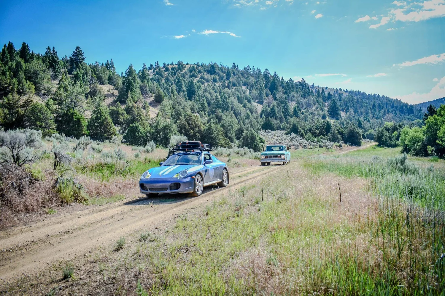 Blue rally car driving quickly on a Montana dirt road with mountains in the distance
