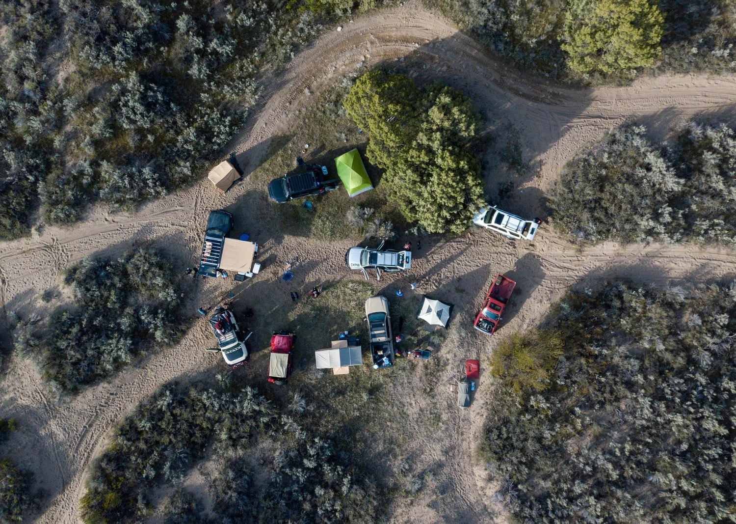 Overhead drone view of a group camp of trucks, tents and a canopy in the sagebrush near the dunes