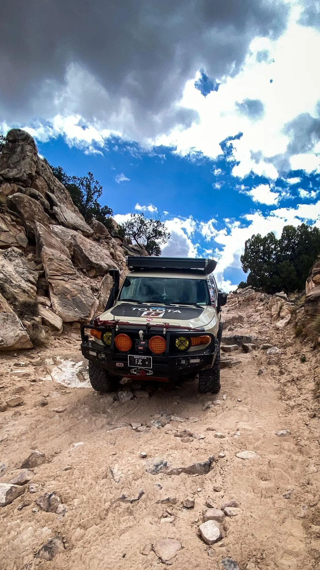 FJ Cruiser driving a rocky canyon trail between red rock walls under dramatic clouds on a spring road trip through Utah