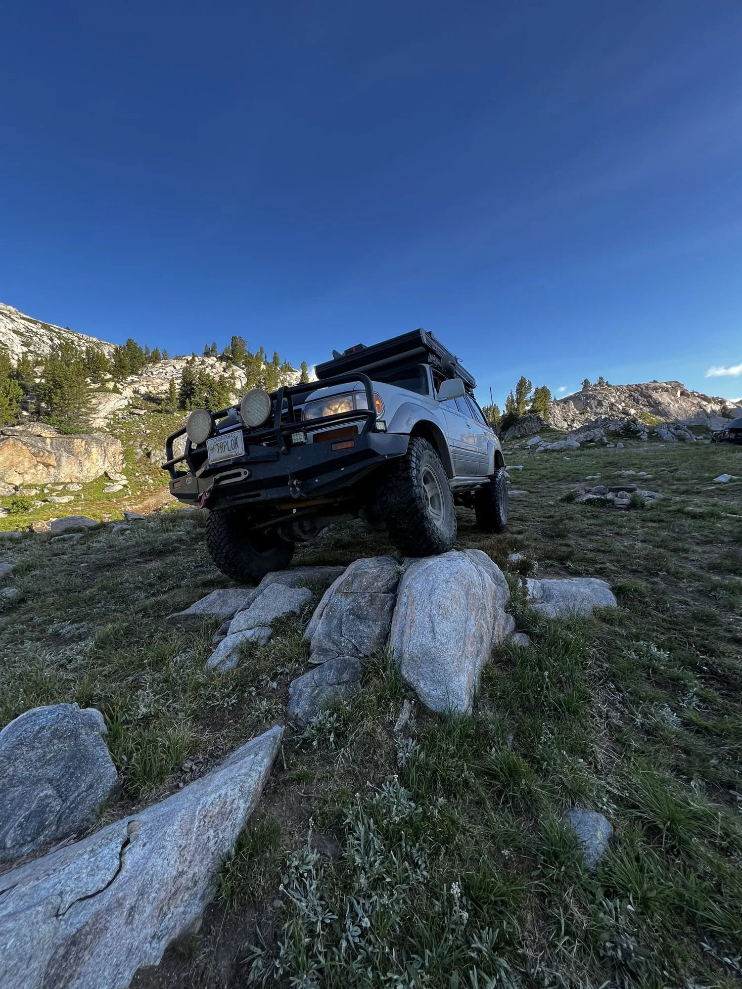 Land Cruiser on a grassy slope among large granite boulders under a deep blue sky near Cooke City, Montana