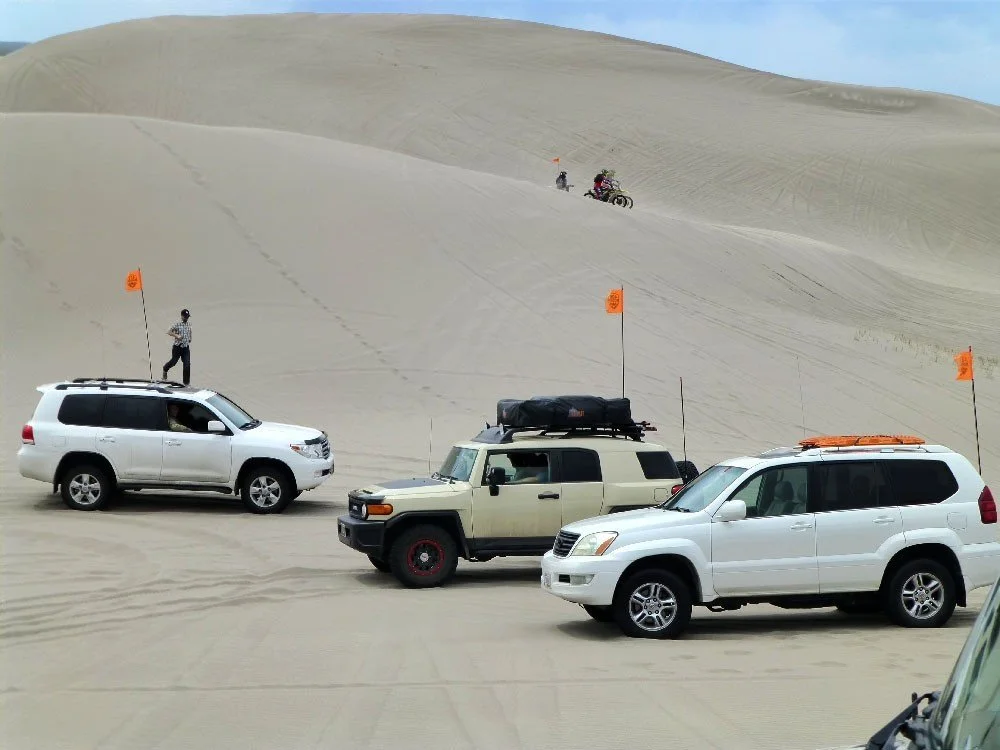 Toyota Land Cruiser 200, FJ Cruiser and Lexus GX parked below a tall dune with people on the slope at the St. Anthony Sand Dunes in Idaho