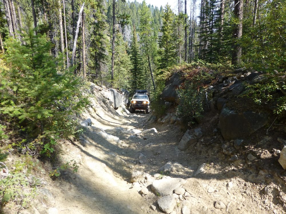 Rocky two-track cut into a hillside through the timber, with a 4x4 ahead, Aug. 26, 2017