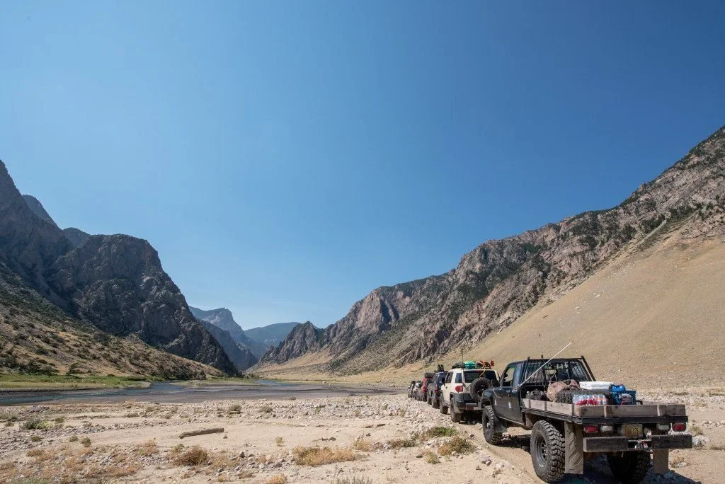 Black flatbed pickup and a line of trucks on the sandy canyon floor below towering rock walls on the Morrison Jeep Trail in Clarks Fork Canyon near Cody, Wyoming