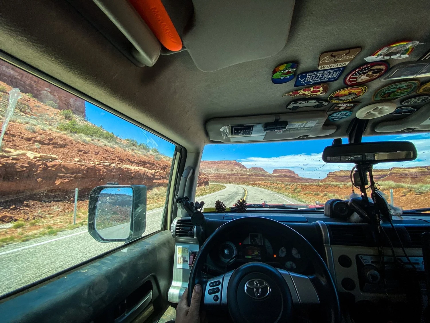View through an FJ Cruiser windshield of a highway running through red rock cliffs on a spring road trip through Utah