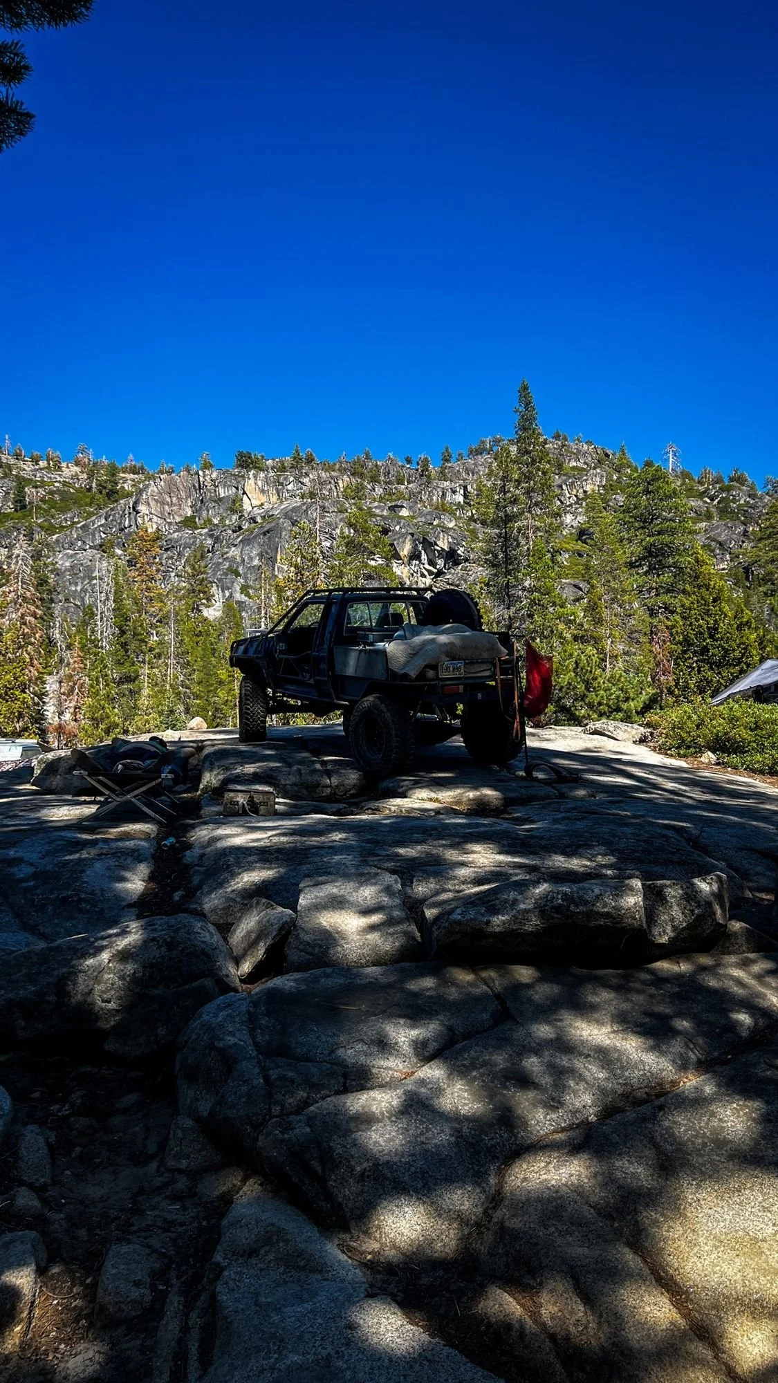 Truck on top of rounded granite under a deep blue sky with a cliff behind on the Rubicon Trail in California during Rubithon 2022