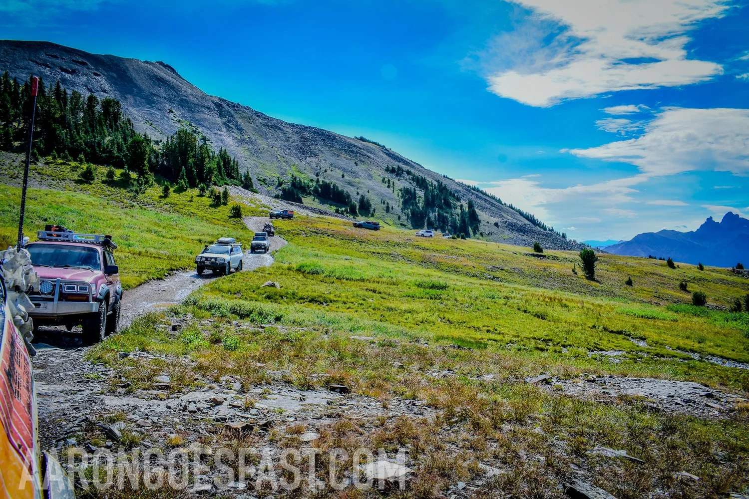 Red 80 Series Toyota Land Cruiser leading a line of Land Cruisers through an alpine meadow on the 406 Cruisers Goose Lake run near Cooke City, Montana