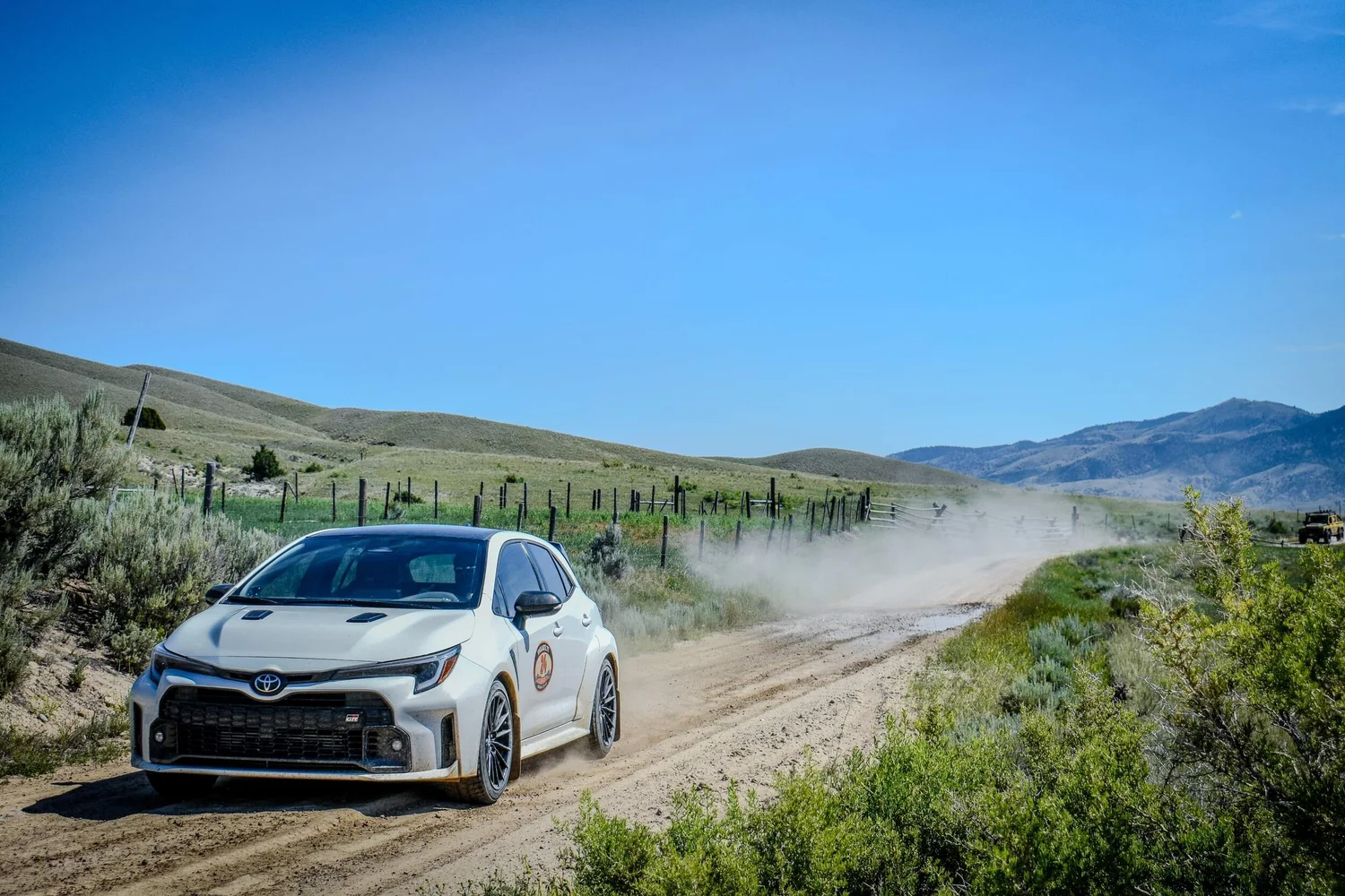 White rally car driving quickly on a Montana dirt road
