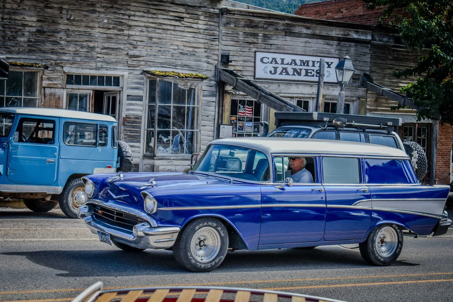 Blue Toyota FJ40 Land Cruiser parked on the main street of Virginia City, Montana, as a blue 1957 Chevrolet wagon drives past during the Vigilante 77 Rally