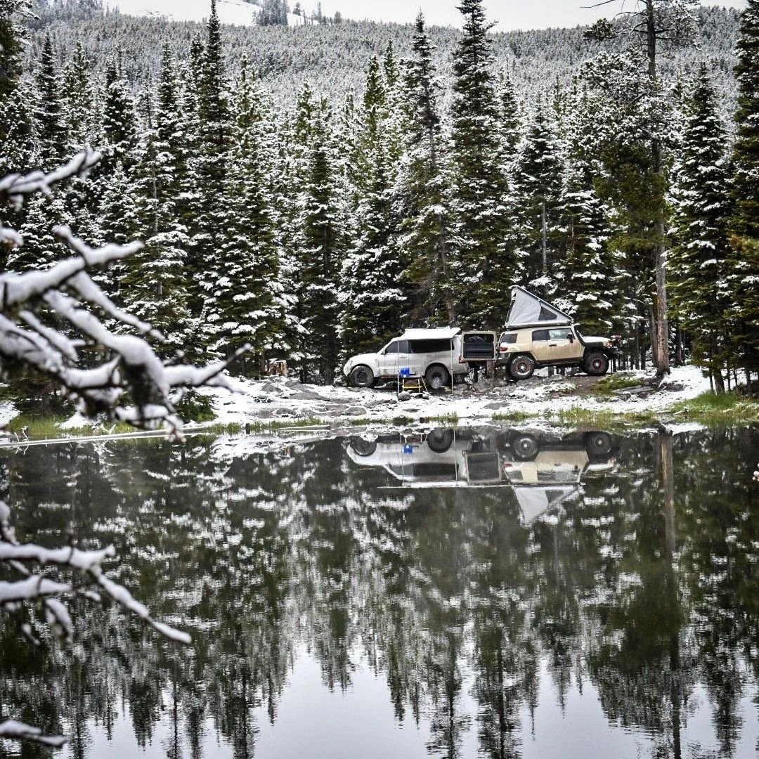 Snowy pine forest and camp reflected in a still lake in the Elkhorn Mountains near Boulder, Montana