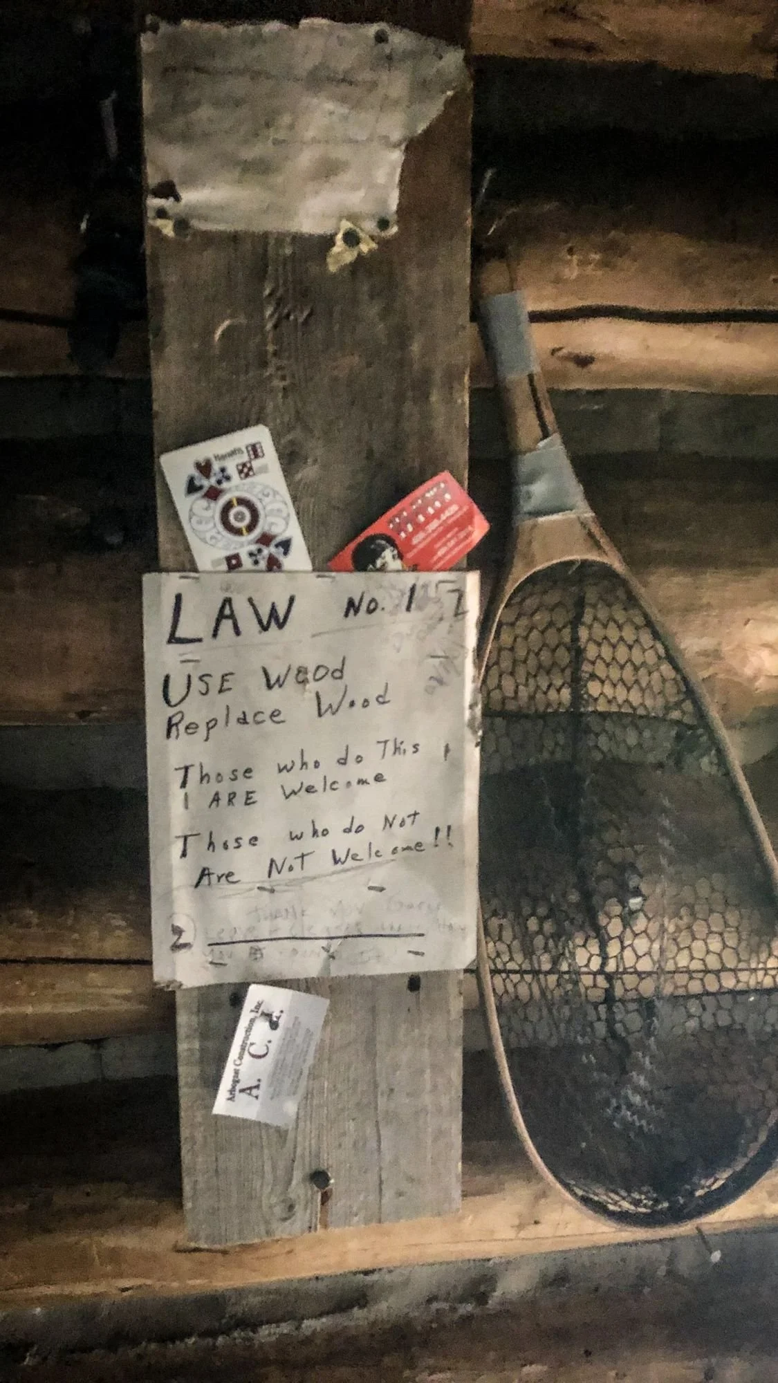 Handwritten Law Number 1 sign reading Use Wood, Replace Wood inside the No Tell Motel cabin next to a fishing net on the North Meadow Creek trail to McKelvey Lake in the Tobacco Root Mountains, Montana