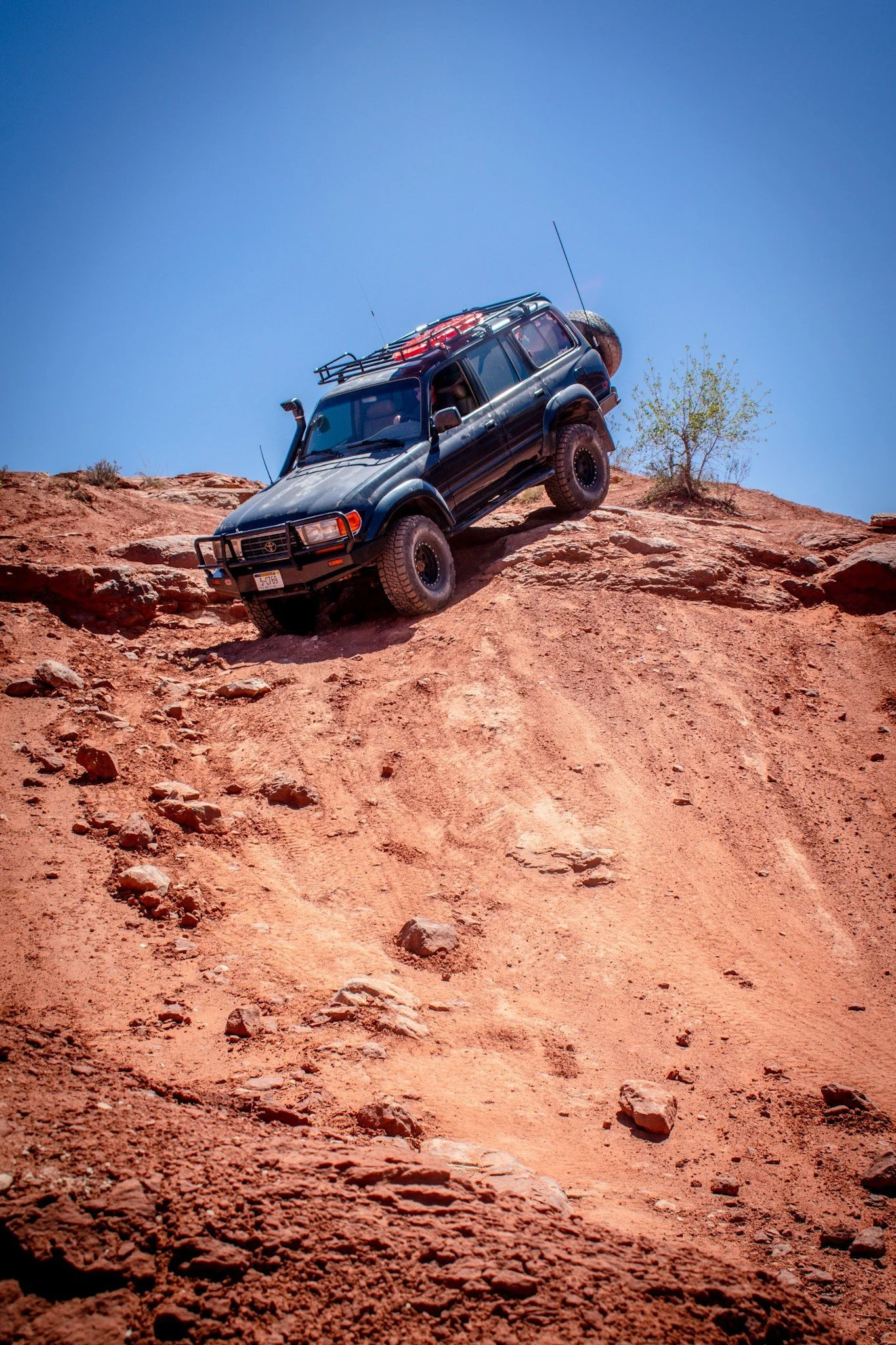 Black Toyota Land Cruiser 80 Series with a snorkel and roof basket nose-down on a steep red-rock ledge on the Seven Mile Rim trail near Moab, Utah