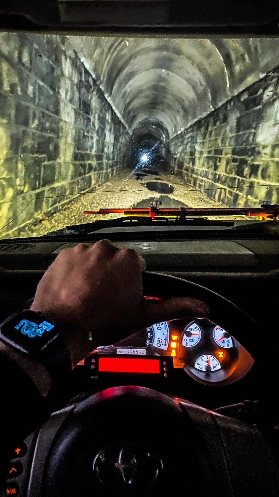 Dashboard view of a driver’s hand on the wheel while driving through the lit, stone-lined Wickes tunnel at the Wickes railroad tunnel near Jefferson City, Montana