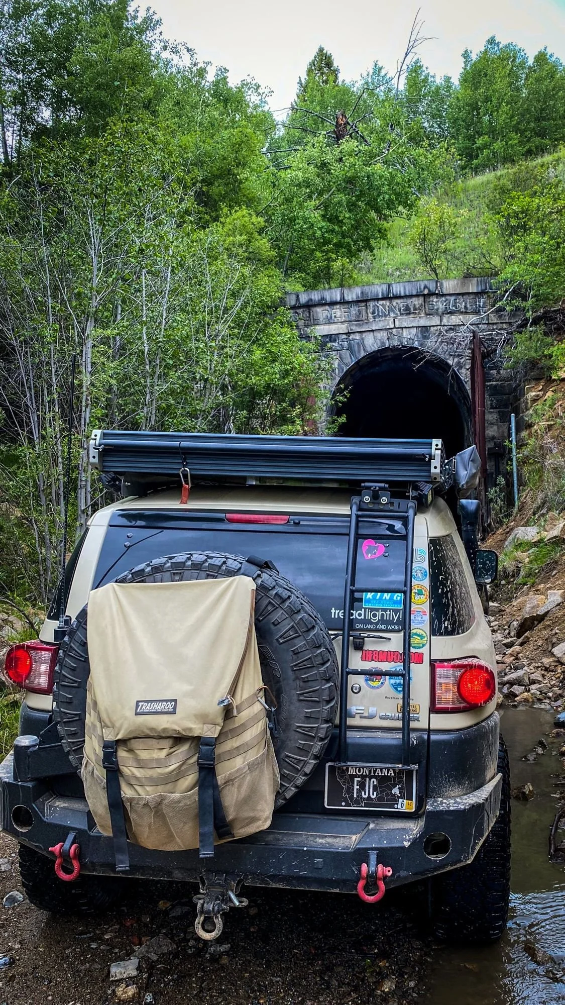 Rear of a tan Toyota FJ Cruiser close to the Wickes tunnel portal, surrounded by brush and timber at the Wickes railroad tunnel near Jefferson City, Montana