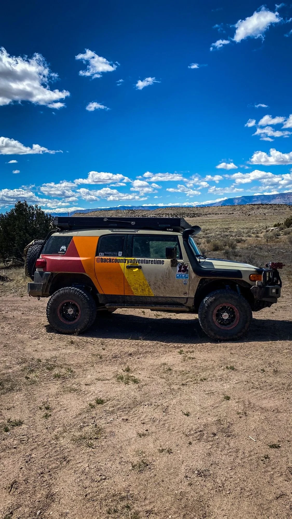 Striped FJ Cruiser parked on a dusty flat under a blue sky with puffy clouds on a spring road trip through Utah