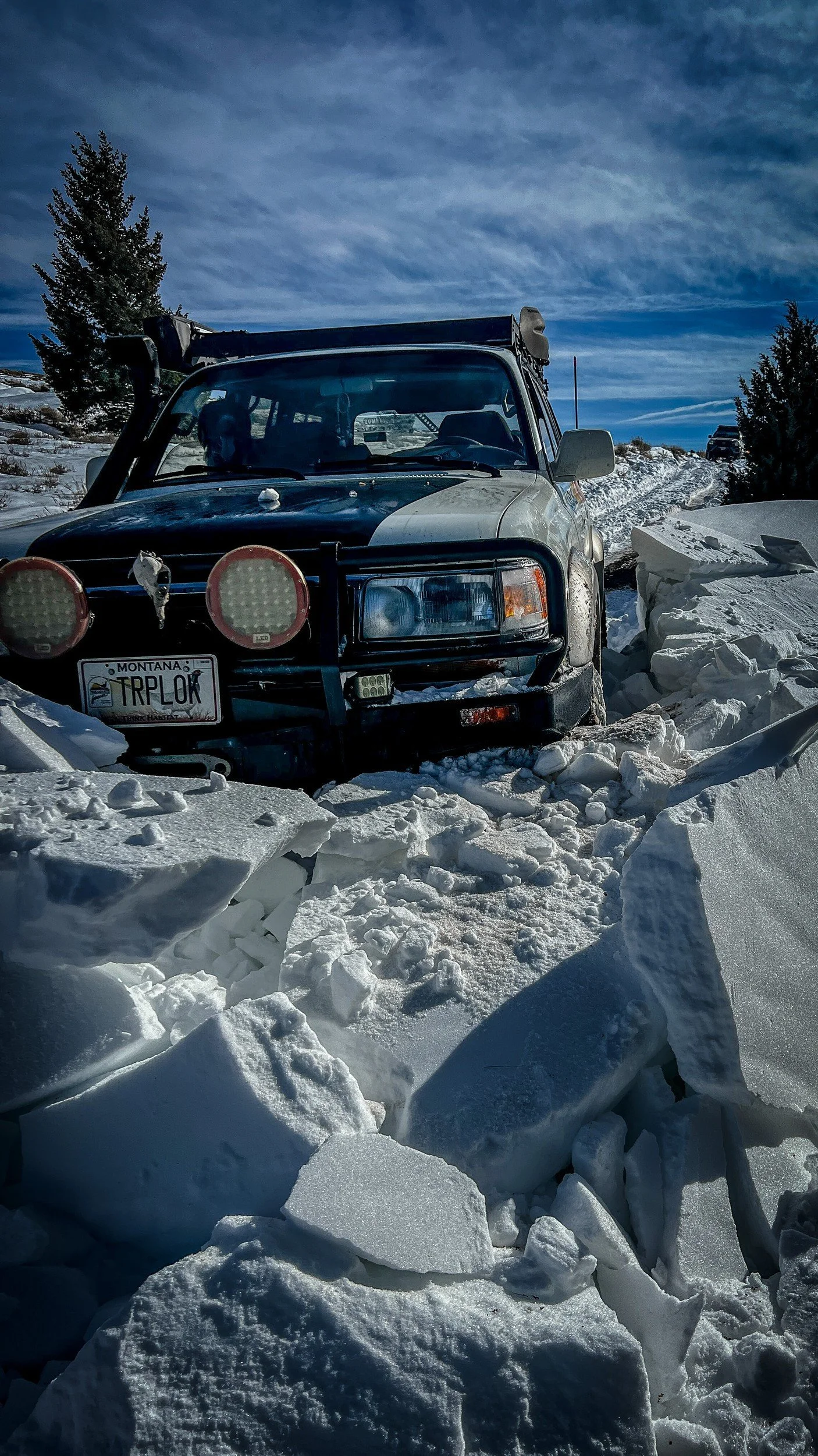 Silver Lexus LX450 TRPLOK with red round lights sitting in broken slabs of wind-crusted snow during a February snow wheeling run in Montana