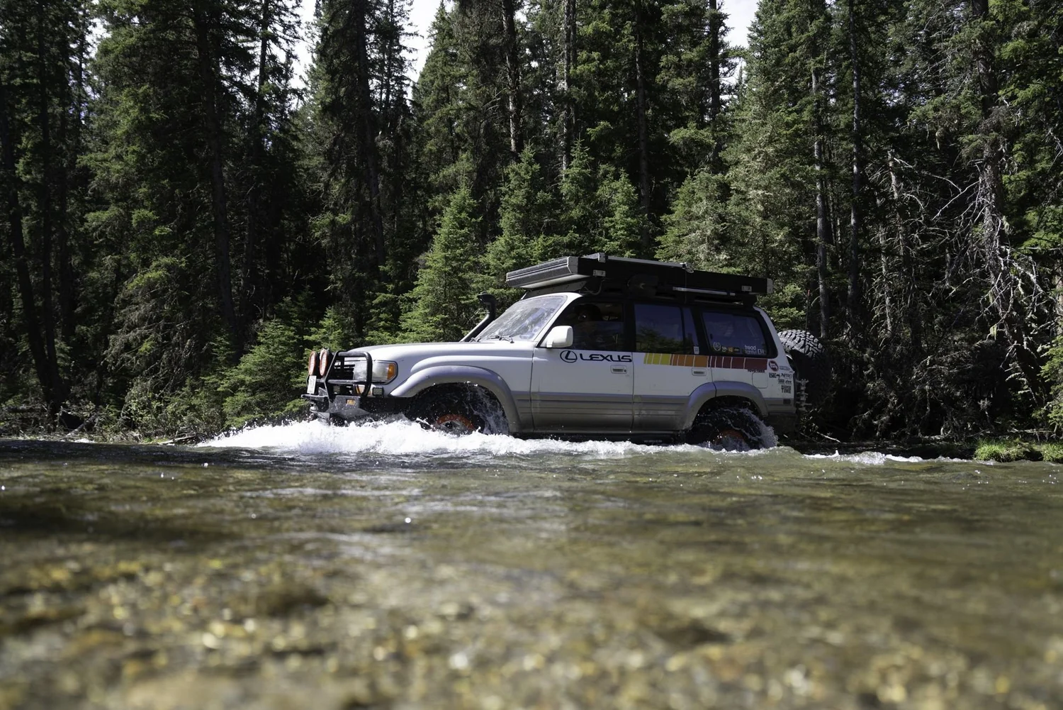 Silver Lexus LX450 crossing a river side-on with a splash on the Middle Fork Judith River road in the Little Belt Mountains, Montana