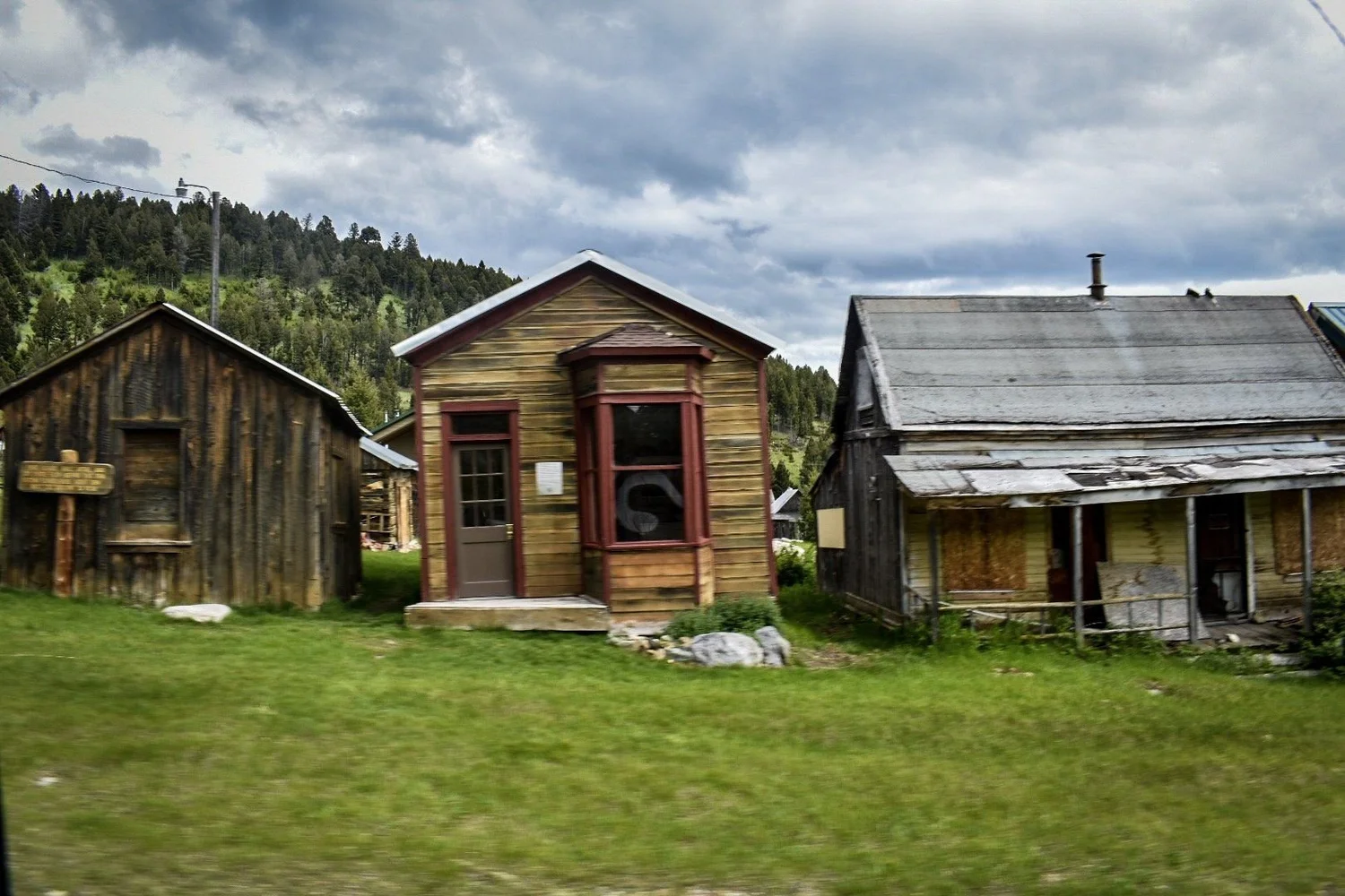 Row of weathered wooden houses with false fronts and porches in a green meadow in Elkhorn, Montana